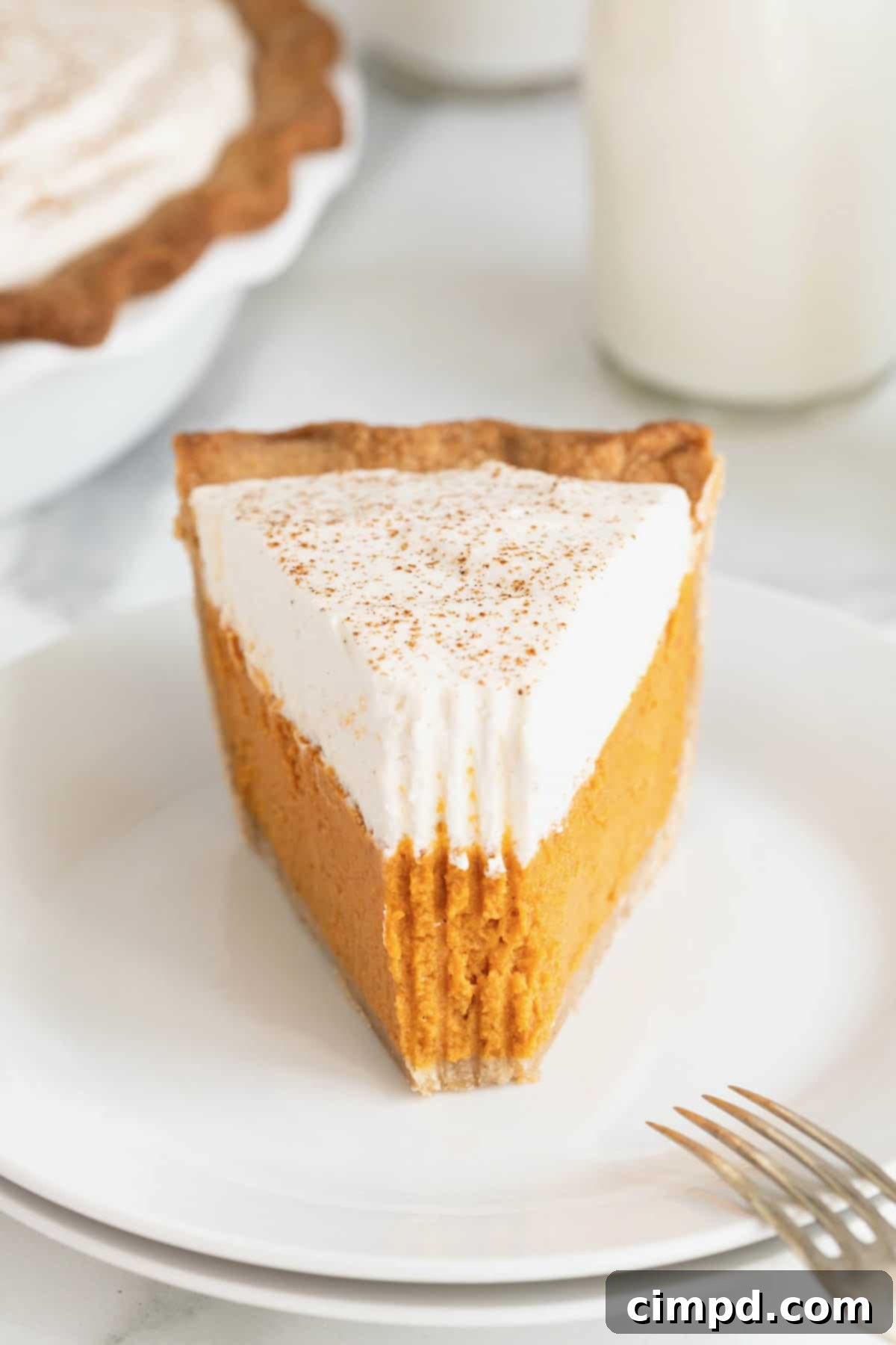A piece of pumpkin cream pie on a small white dessert plate with a bite taken out of it.