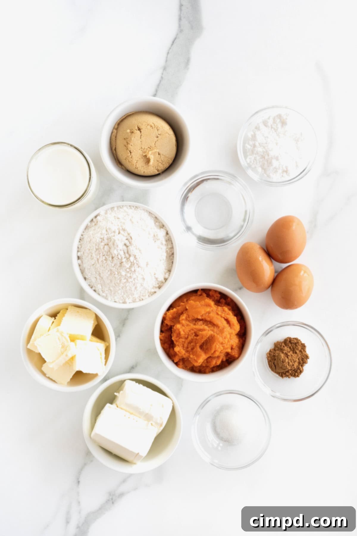 Ingredients to make a pumpkin cream pie in small glass dishes on a white marble counter.