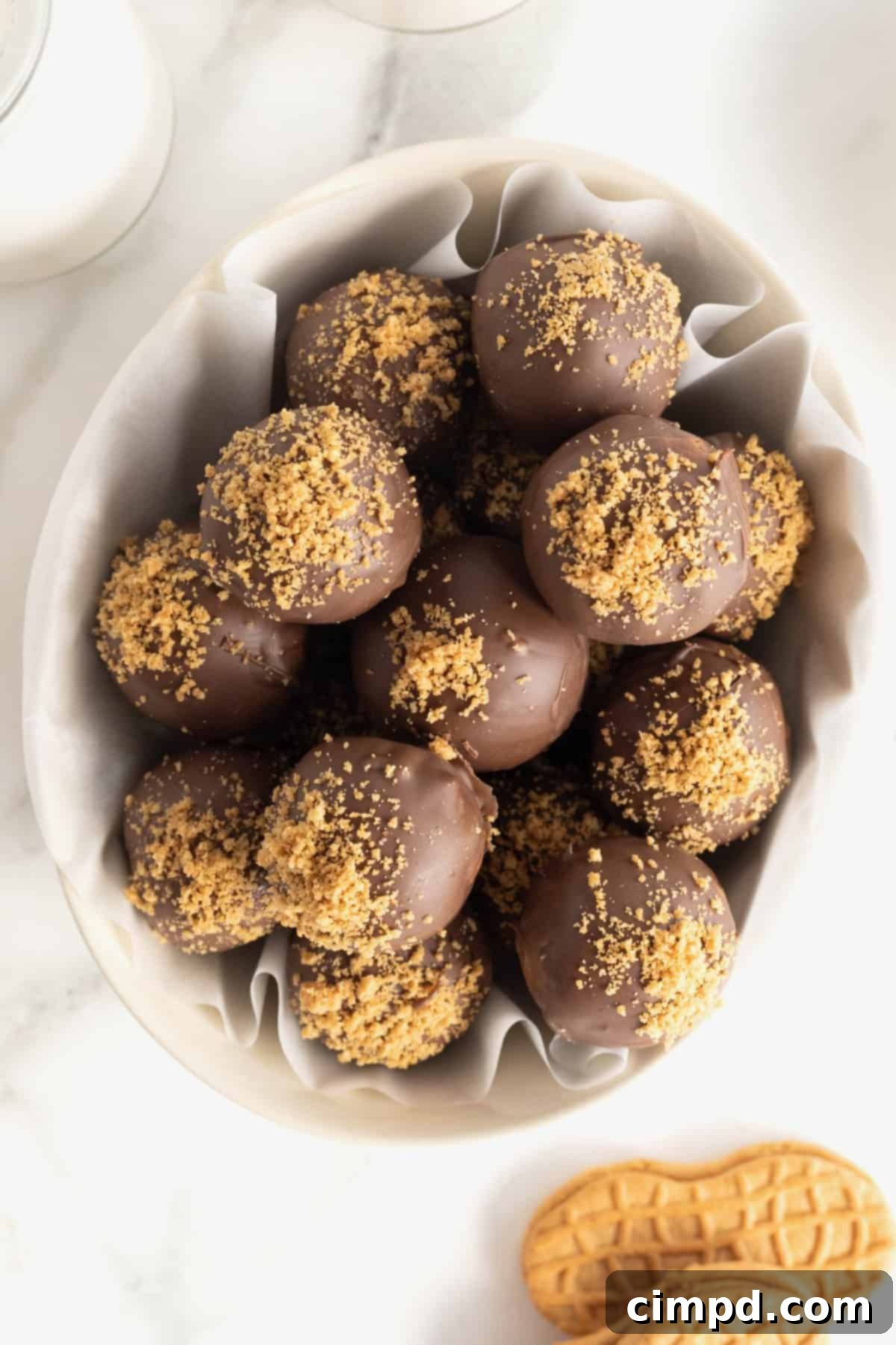A white, oblong, parchment-lined serving dish filled with chocolate covered Nutter Butter balls, dusted with cookie crumbs.