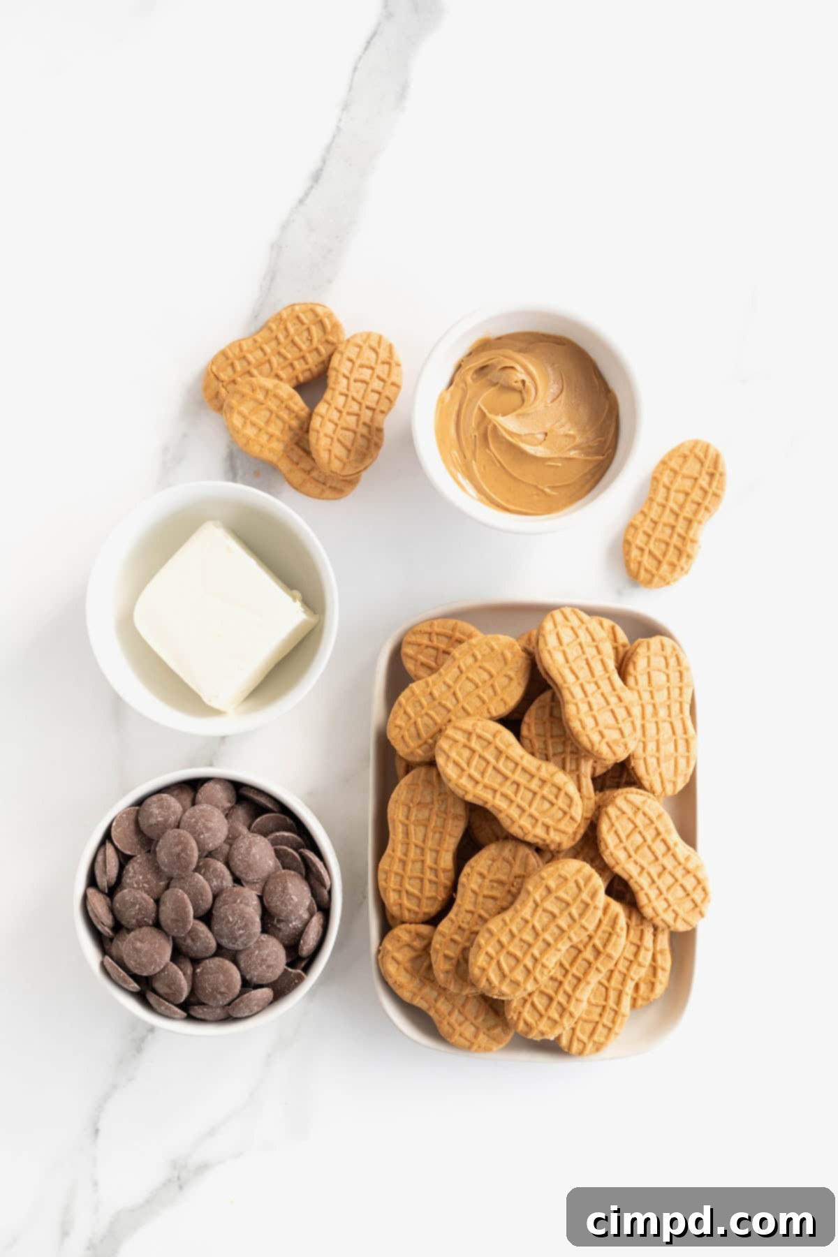 Ingredients laid out on a white marble counter for making Nutter Butter Balls in small white dishes.