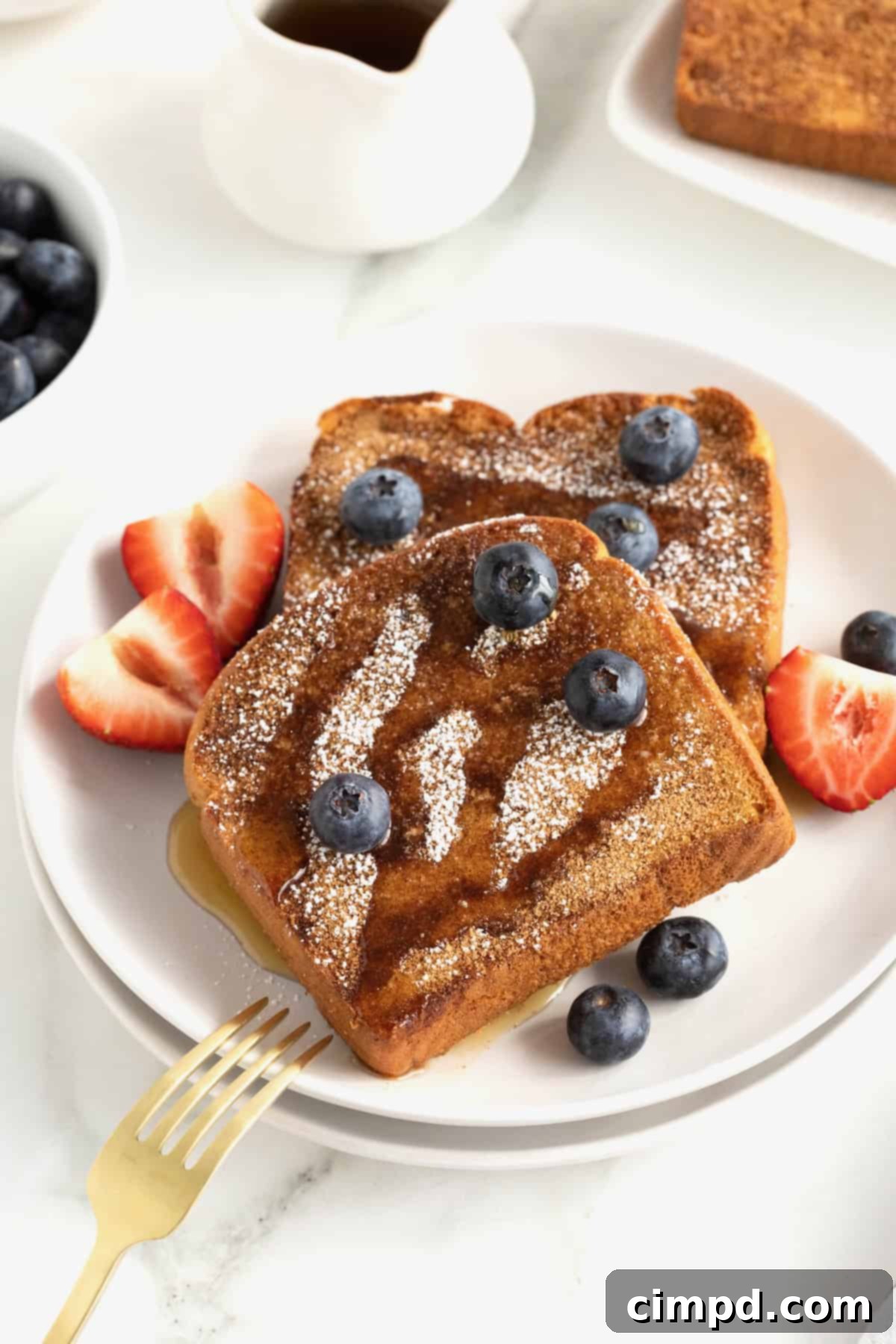 A white plate of three pieces of baked French toast topped with maple syrup and berries.