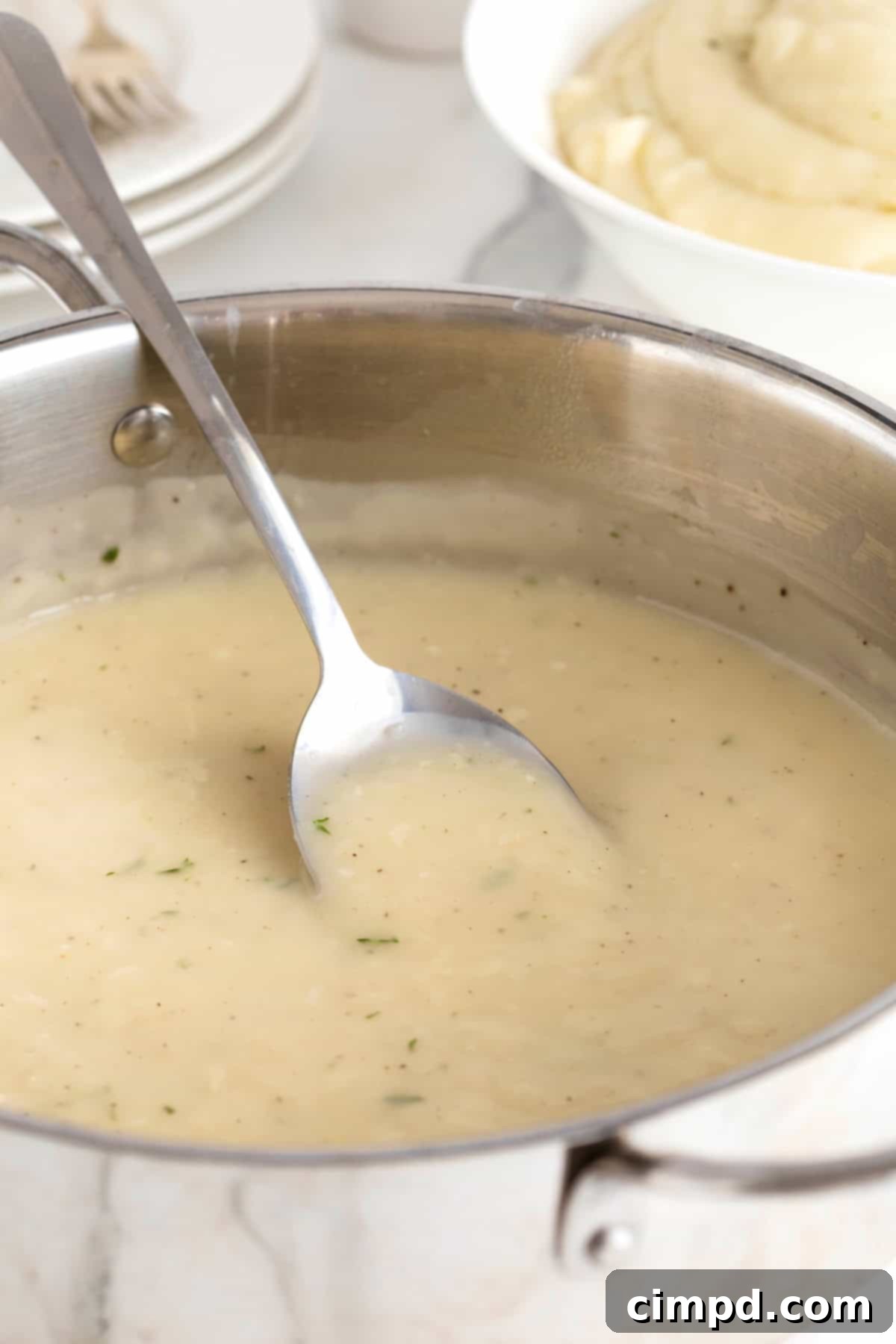 A metal spoon resting inside a stainless steel pot filled with bubbling, aromatic turkey gravy, showcasing its rich texture and color.