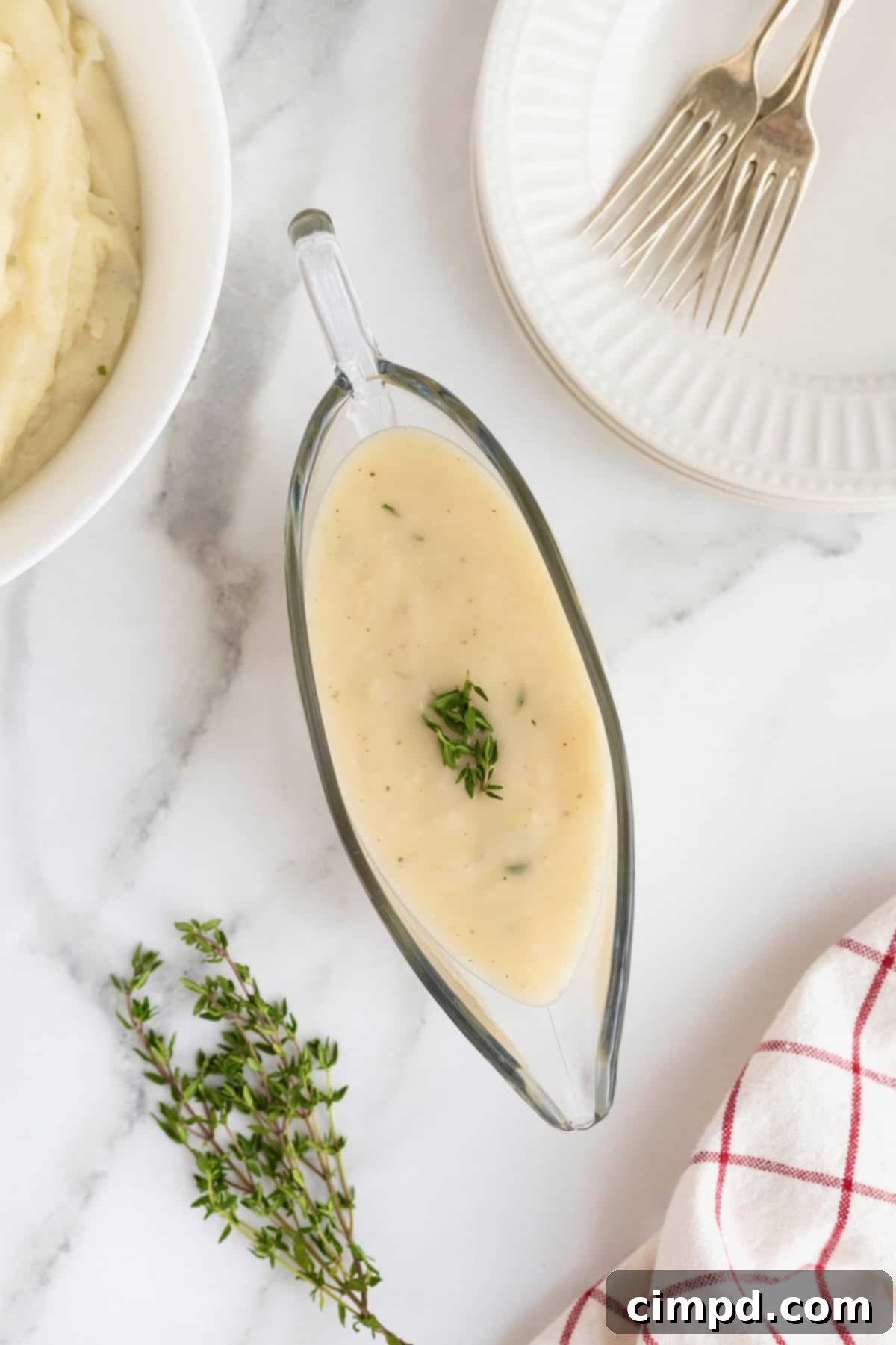 A glass gravy boat overflowing with homemade turkey gravy, gracefully placed on a white marble counter. A large white serving bowl of creamy mashed potatoes is visible in the soft background, inviting a delicious pairing.