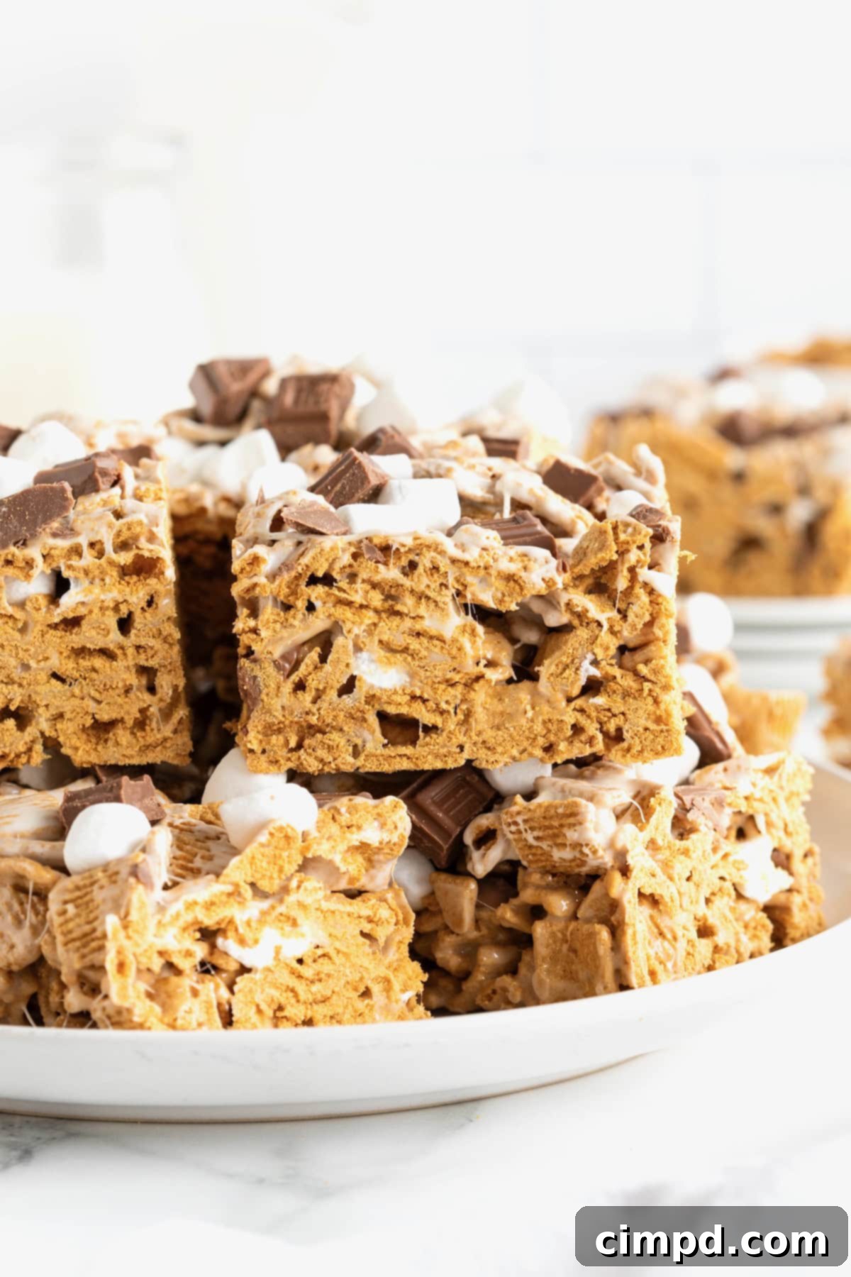 Easy No Bake Smores Bars 2 A large white rimmed plate stacked with golden brown No-Bake S'mores Bars, showcasing their melty chocolate and marshmallow layers.