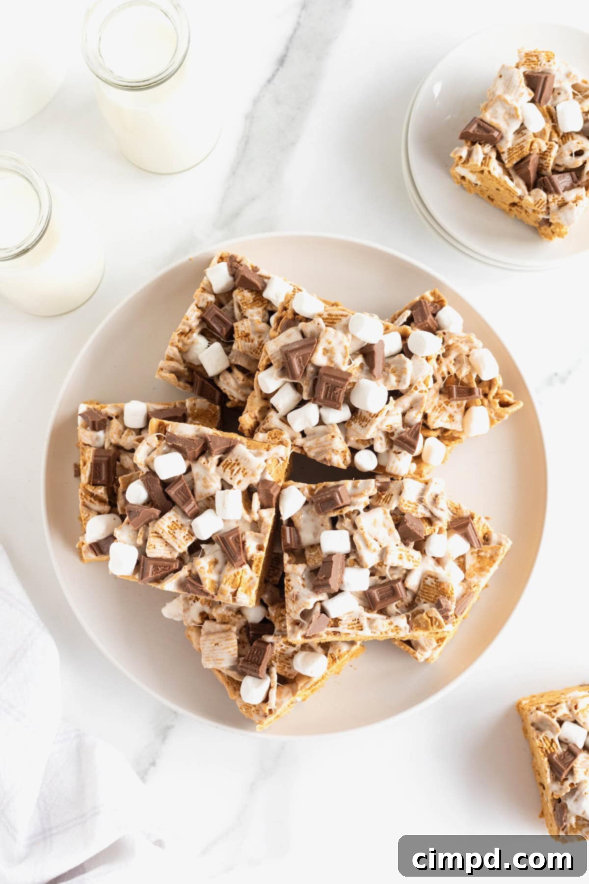 Easy No Bake Smores Bars 4 A large white plate generously stacked with freshly made No-Bake S'mores Bars on a pristine white counter, ready to be enjoyed.