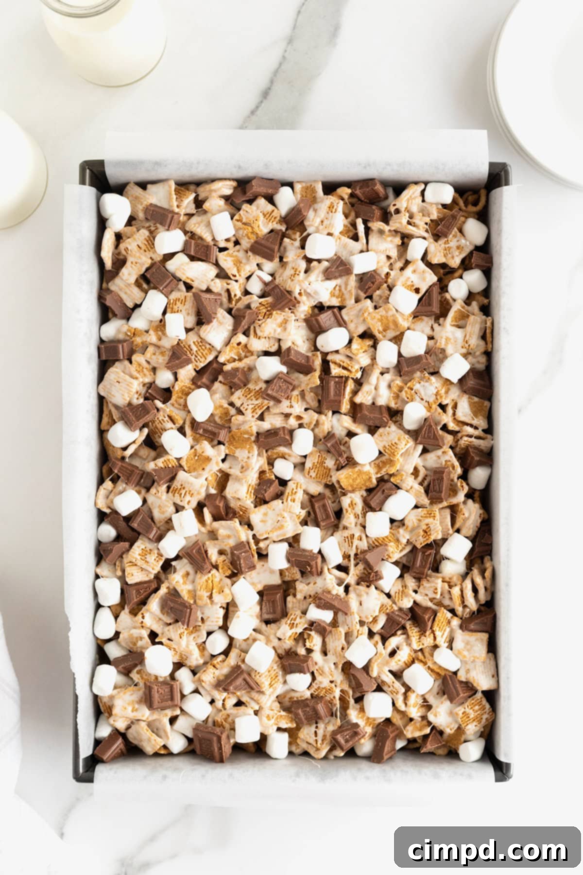 Easy No Bake Smores Bars 9 A parchment-lined baking pan filled with a freshly prepared batch of No-Bake S'mores Bars, ready for cooling and cutting.