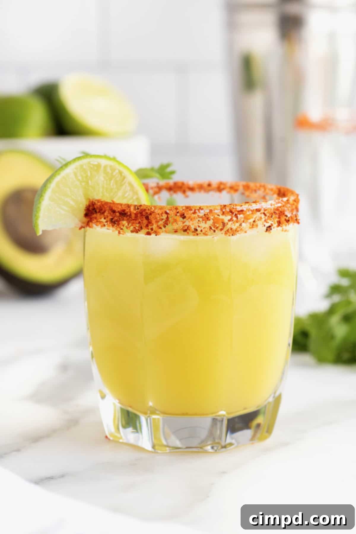 A short glass filled with a vibrant green avocado margarita, rimmed with a spicy Tajín seasoning, and garnished with a fresh lime wedge.