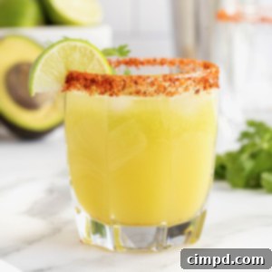A short glass filled with a vibrant green avocado margarita, rimmed with a spicy Tajín seasoning.