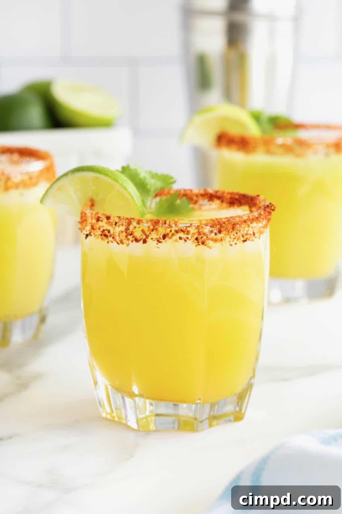 Three perfectly crafted avocado margaritas arranged artfully in short glasses, each rimmed with a vibrant chili-lime seasoning and elegantly garnished with fresh cilantro and a bright lime wedge.