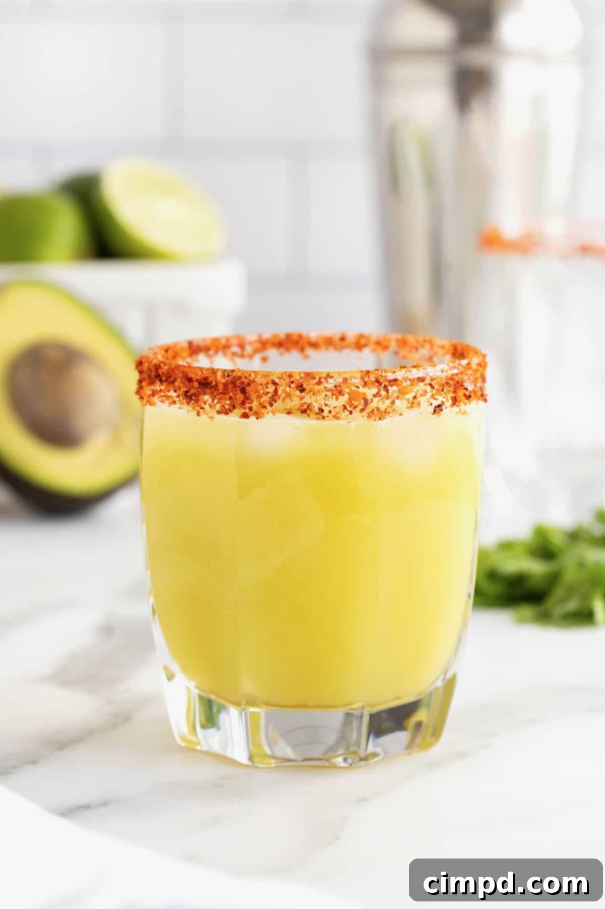 A close-up of a single avocado margarita in a stylish glass, featuring a rim generously coated with Tajín seasoning, showcasing its vibrant green color and inviting texture.