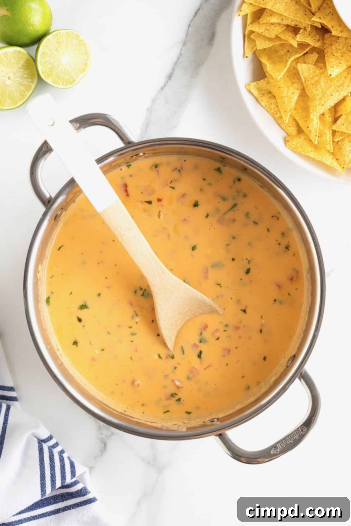 A wooden spoon rests peacefully in a large, polished stainless steel pot filled with rich, creamy queso, inviting a taste of its deliciousness.