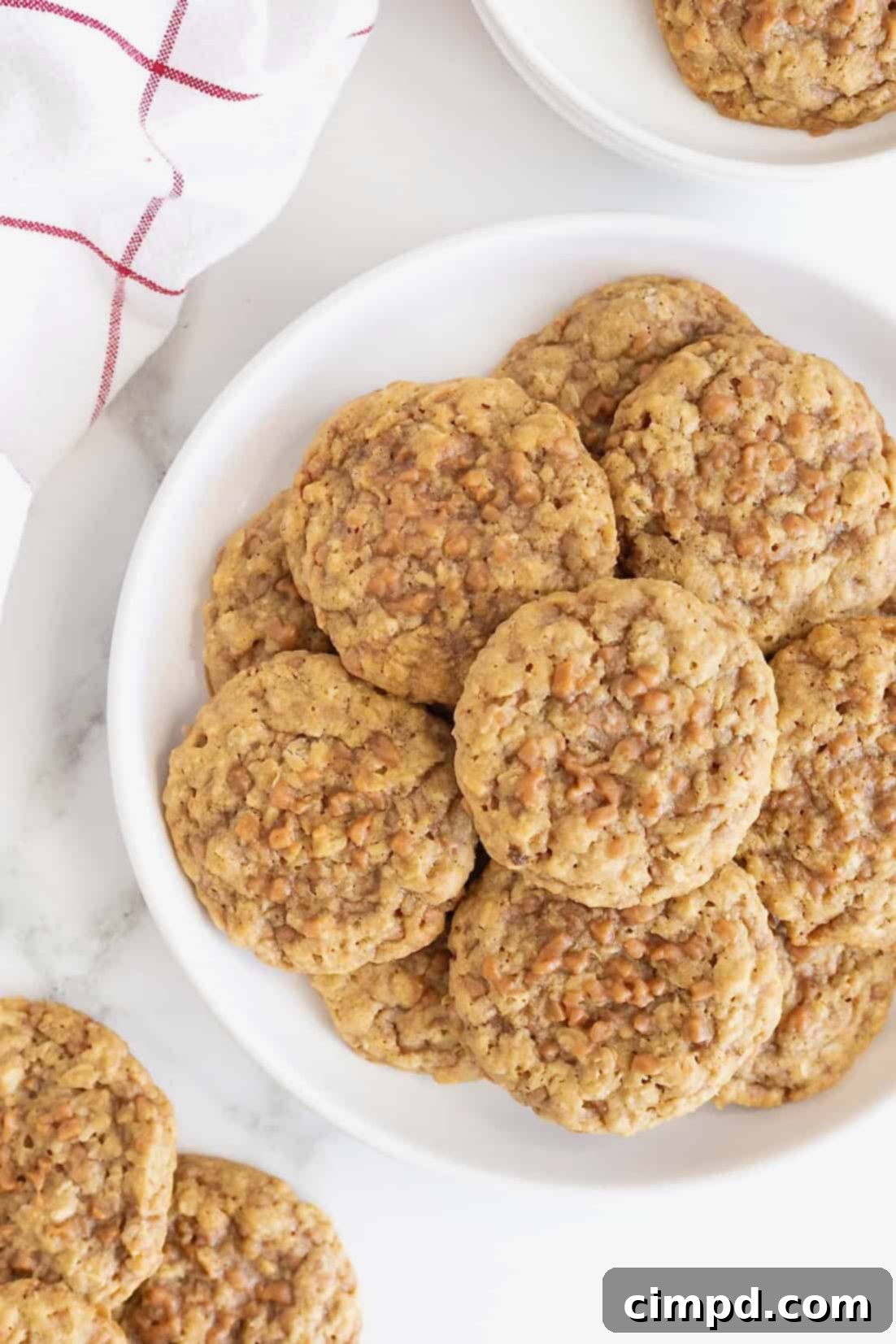A large white plate brimming with freshly baked Brown Sugar Oatmeal Toffee Crunch Cookies on a elegant white marble countertop, suggesting a cozy kitchen setting.