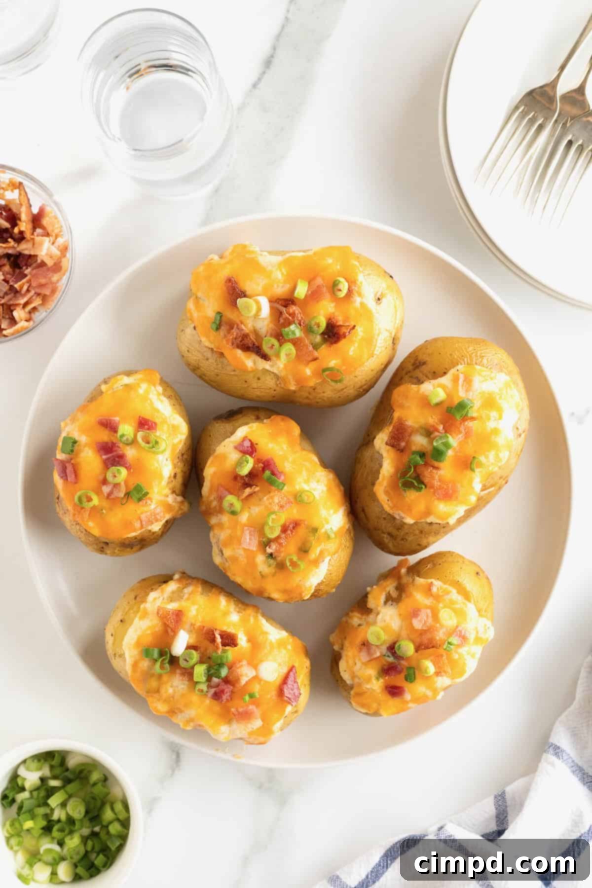 A large white serving plate displaying beautifully golden-brown twice baked potatoes, abundantly topped with crispy bacon pieces, vibrant green onion, and melted cheddar cheese.
