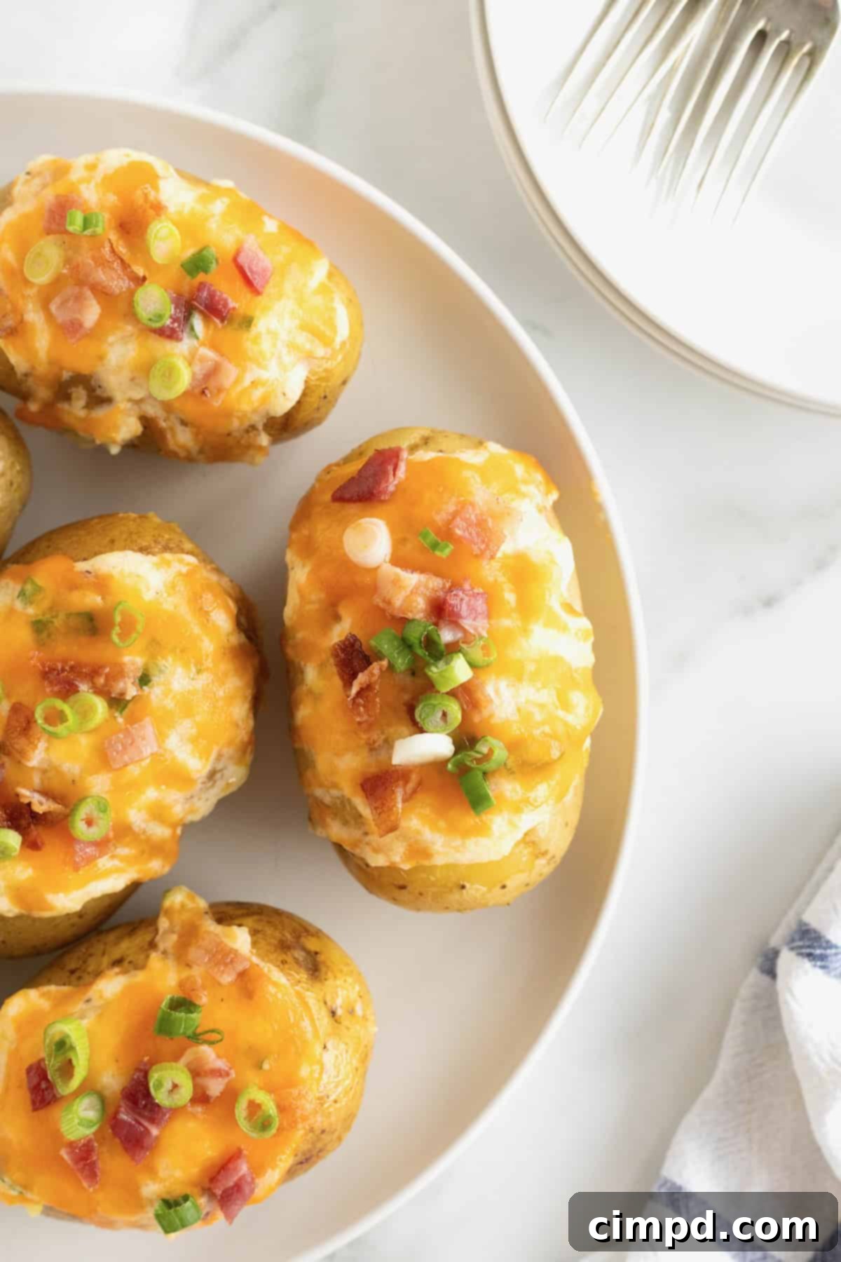 A generous white rimmed plate showcasing four perfectly crafted twice baked potatoes, arranged elegantly on a clean white marble counter, ready for serving or storage.