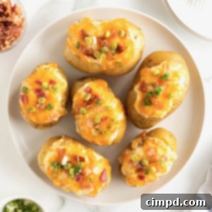 A large white serving plate of twice baked potatoes loaded with bacon pieces, green onion and cheddar cheese.
