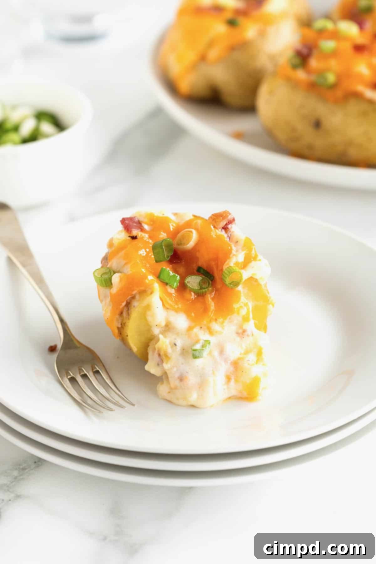 A single, perfectly golden-brown twice baked potato resting on a small white plate, accompanied by a metal fork to the left, ready to be enjoyed.