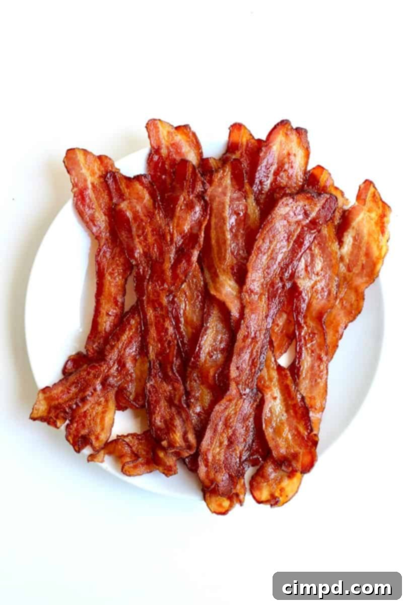 A close-up shot of perfectly baked bacon strips arranged on a baking sheet, showcasing their crisp texture and golden-brown color, with the title 'How to Bake Bacon by The BakerMama' overlaid.