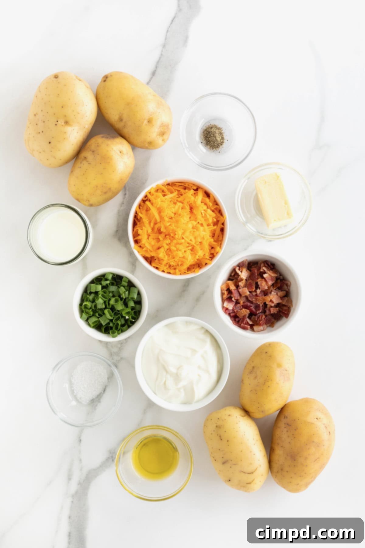 A beautiful arrangement of fresh ingredients for twice baked potatoes, meticulously placed in small glass dishes on a pristine white marble counter, ready for preparation.