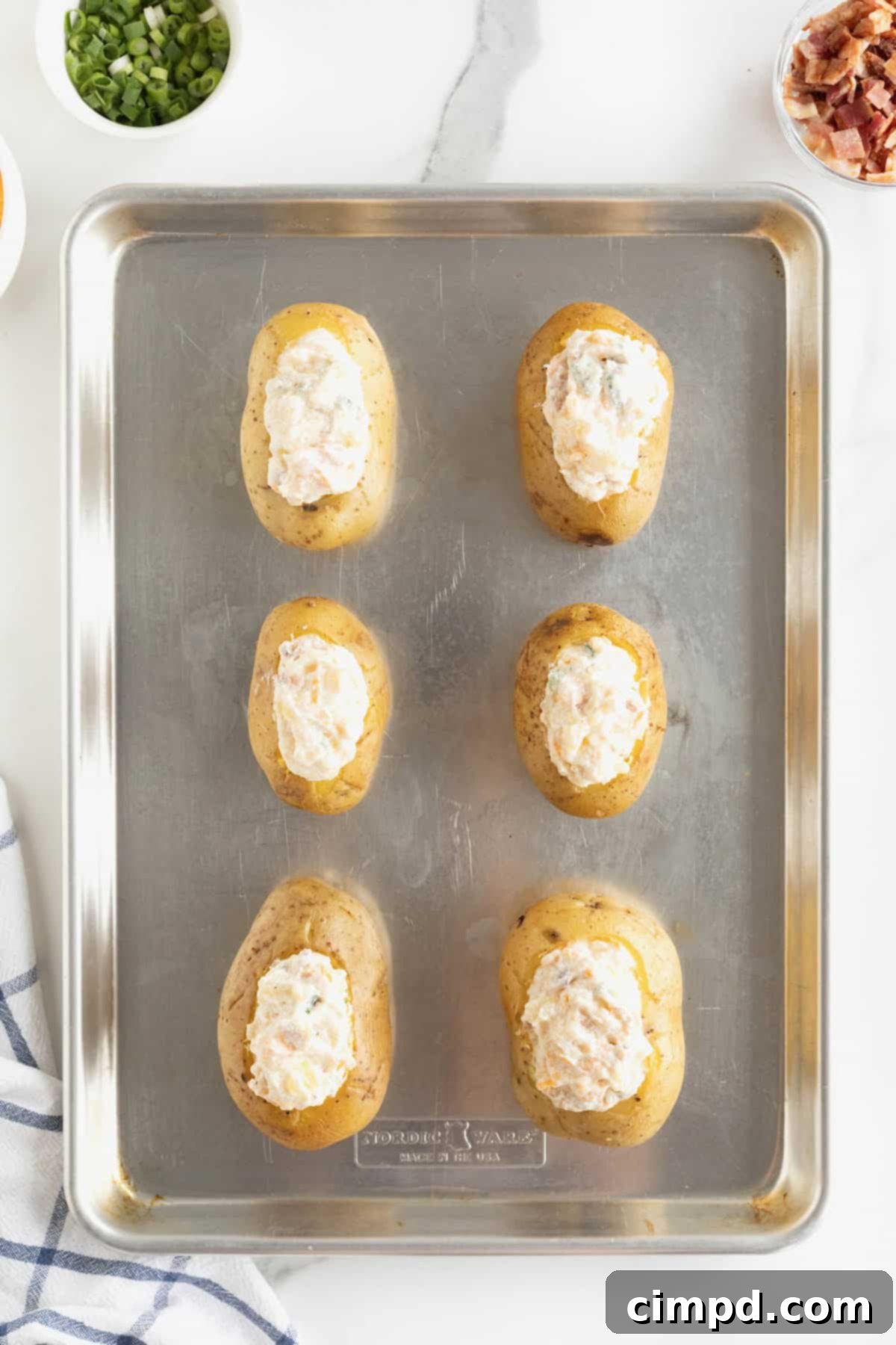Six beautifully filled twice baked potatoes, with their creamy, mounded filling, neatly arranged on an aluminum baking sheet, ready for the final bake.
