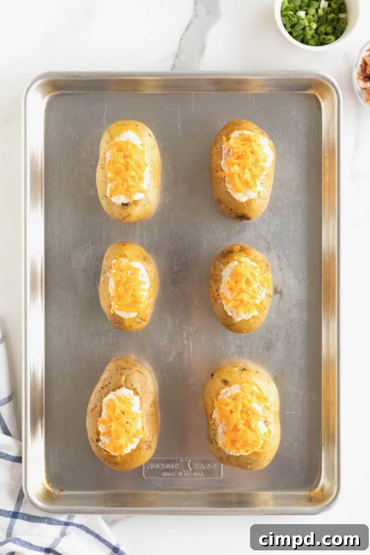 Six twice baked potatoes on an aluminum baking sheet, showcasing beautifully melted and slightly browned cheddar cheese on top after their final bake.