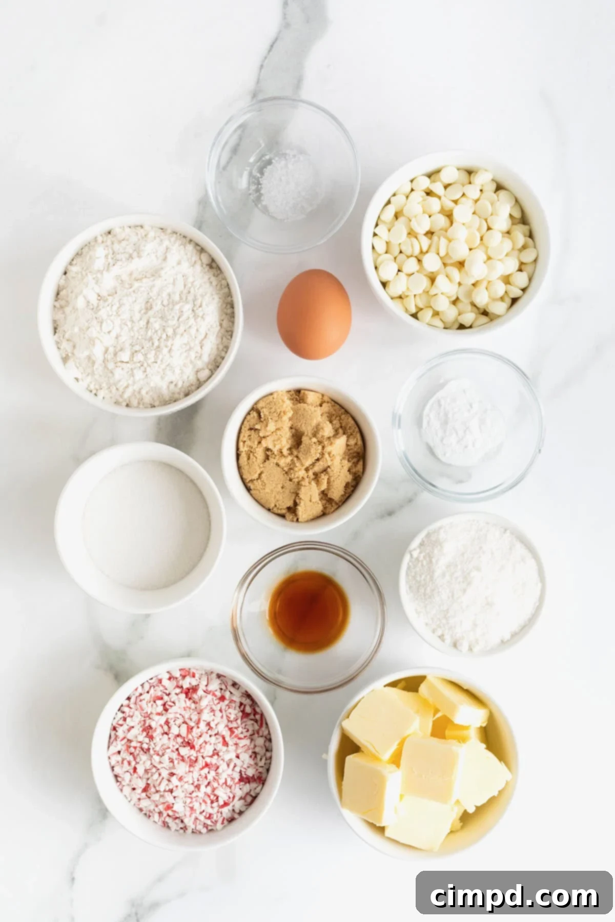 Dreamy Peppermint White Chocolate Pudding Cookies 6 A beautiful arrangement of ingredients for peppermint white chocolate cookies, neatly laid out in small white and elegant glass dishes on a pristine white marble counter, ready for baking.