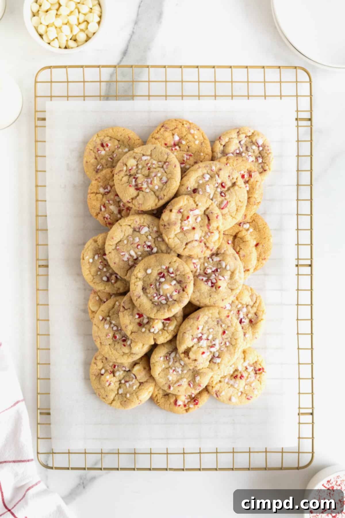 Dreamy Peppermint White Chocolate Pudding Cookies 10 A generous pile of peppermint white chocolate pudding cookies, beautifully adorned with vibrant peppermint bits and creamy white chocolate, resting on a parchment-lined cooling rack, tempting to eat.