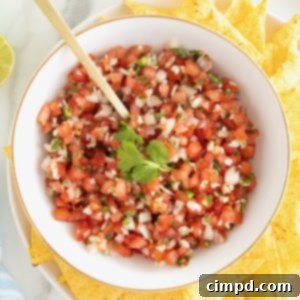 A large white serving bowl of pico de Gallo garnished with a sprig of cilantro. There are tortilla chips surrounding the serving bowl.