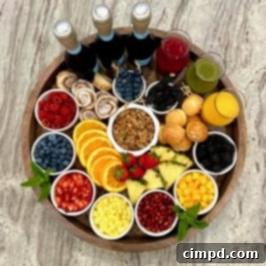 Mimosa Blossom Board 9 A large round, rimmed wood food board filled with colorful fresh fruits in small white dishes, glass carafes of fruit juice and three bottles of Prosecco.