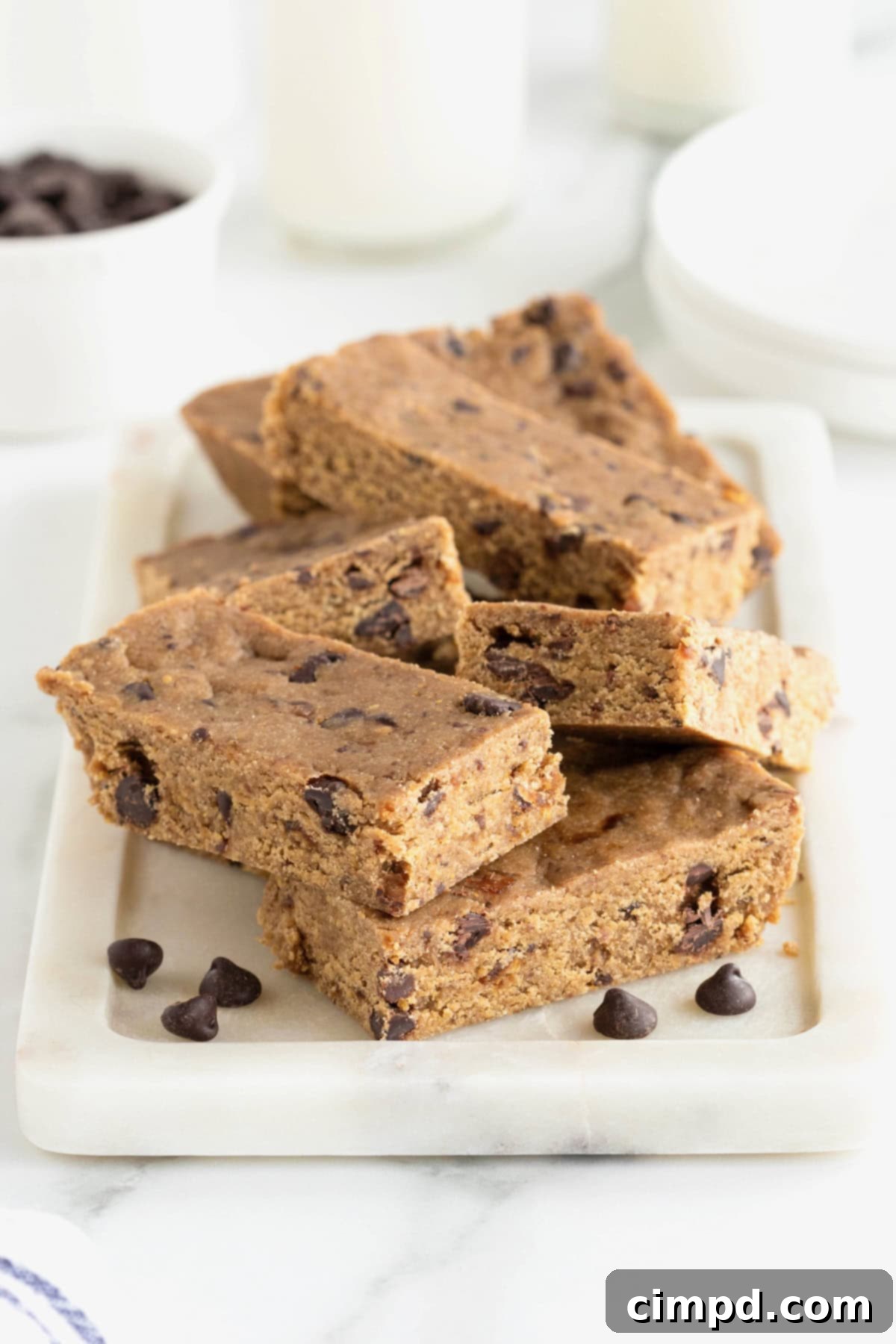 Seven breakfast bars piled on a white, rectangle-shaped board on top of a white marble counter, invitingly arranged.