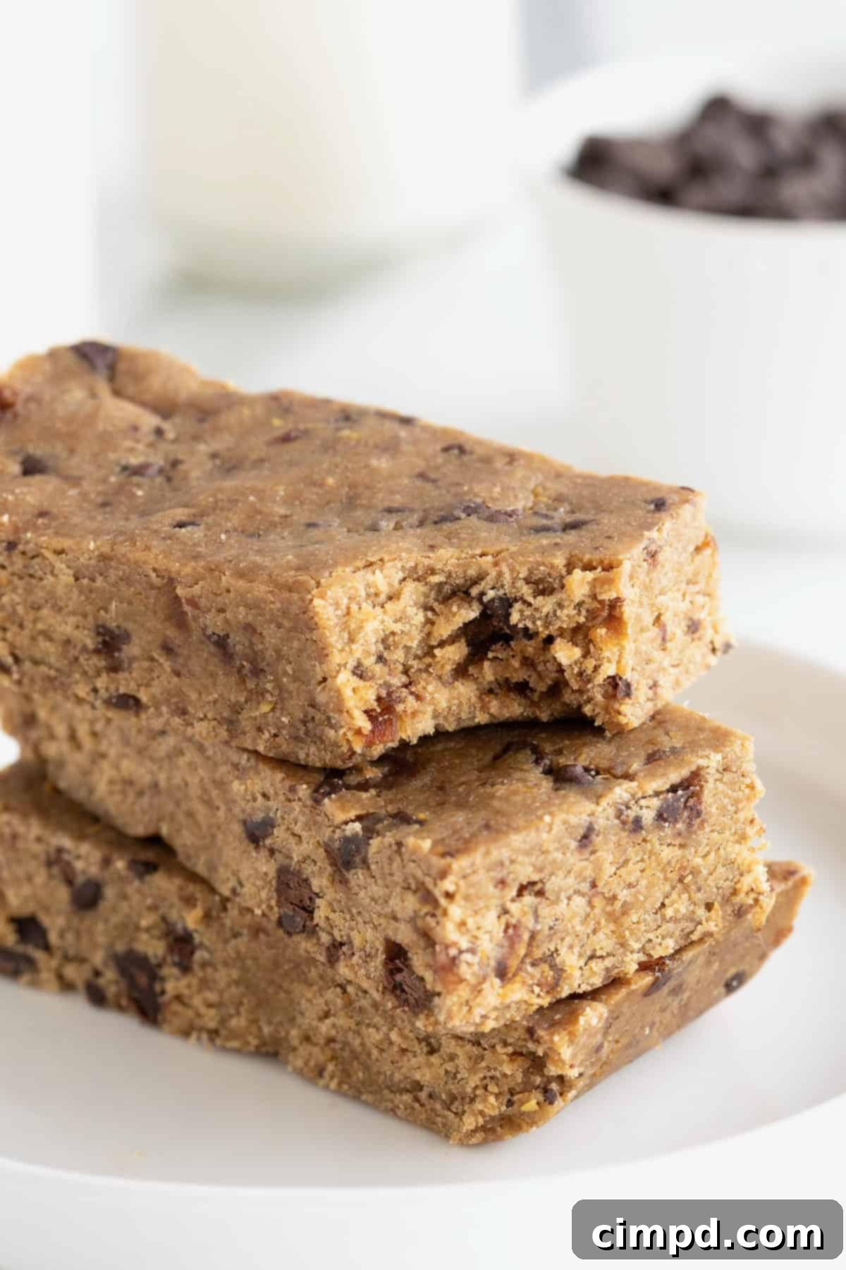 A stack of three peanut butter chocolate chip breakfast bars on a small white plate. The top bar has a bite taken out, revealing the textured interior.