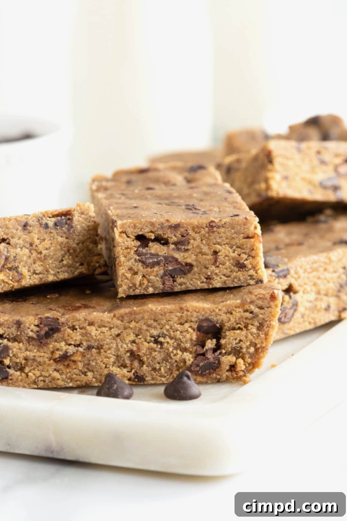 Seven peanut butter chocolate chip breakfast bars perfectly arranged on a white, rectangle-shaped board, sitting on a white marble counter.