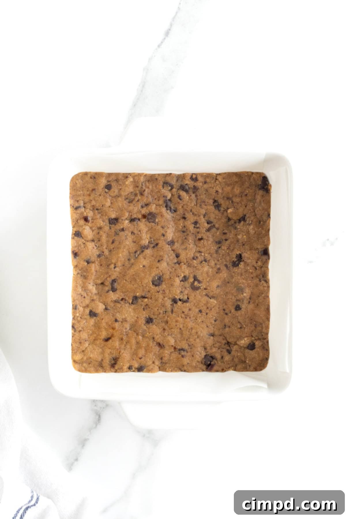 A white glass baking dish with peanut butter chocolate chip breakfast bar dough pressed into it, lined with parchment paper.