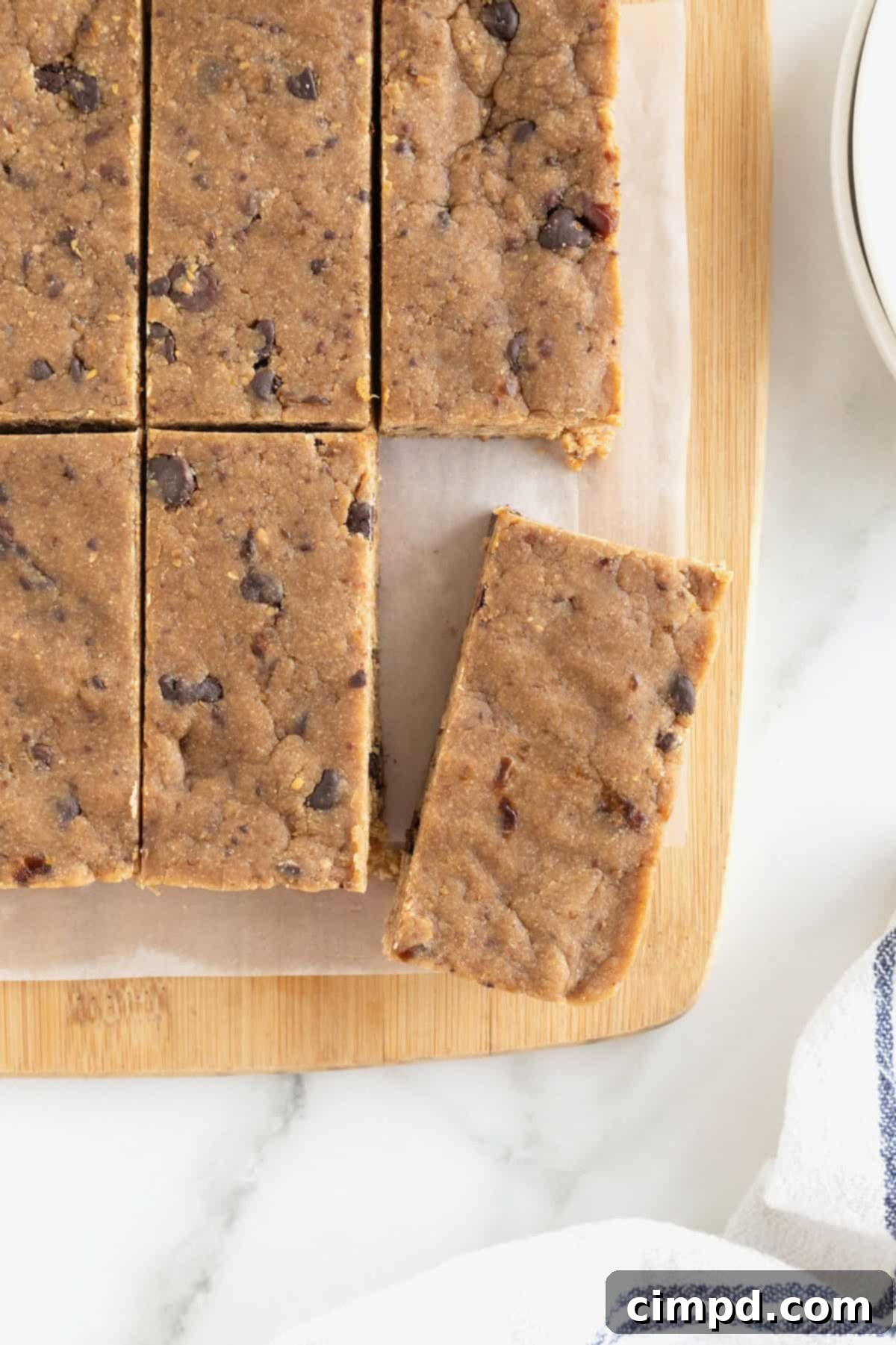 Six peanut butter chocolate chip breakfast bars arranged on a parchment-lined light wood cutting board, showcasing their rich texture.