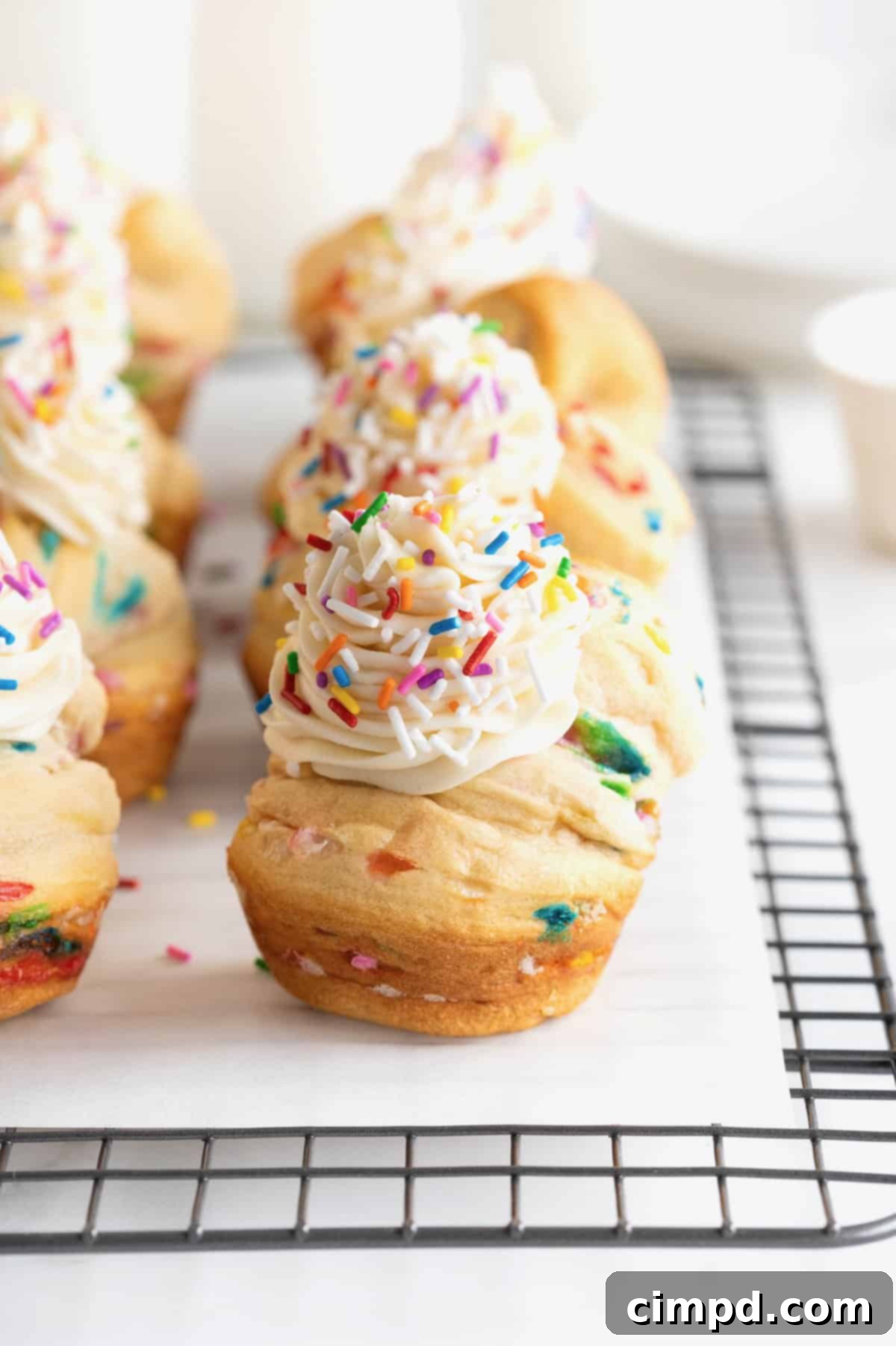 Rainbow Swirl Puffs 11 Six vibrant confetti cruffins, each topped with creamy icing, neatly arranged on a sturdy wire cooling rack.
