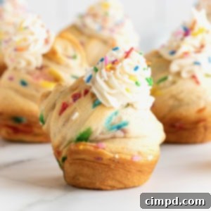 Rainbow Swirl Puffs 14 Rainbow sprinkled cruffins topped with simple icing on a white marble counter.
