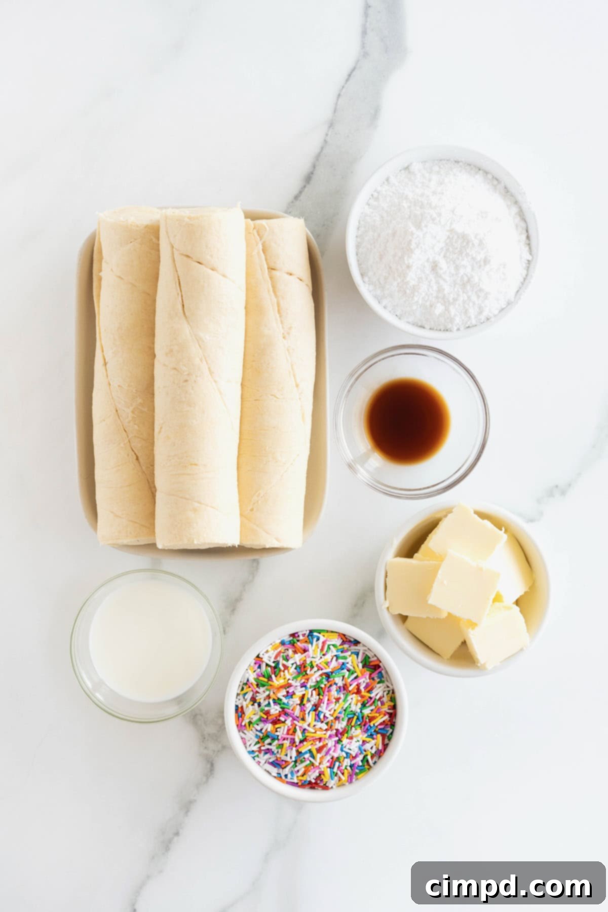 Rainbow Swirl Puffs 5 A beautiful display of all the ingredients needed to make confetti cruffins, neatly arranged in small glass dishes on a pristine white marble counter, ready for baking.