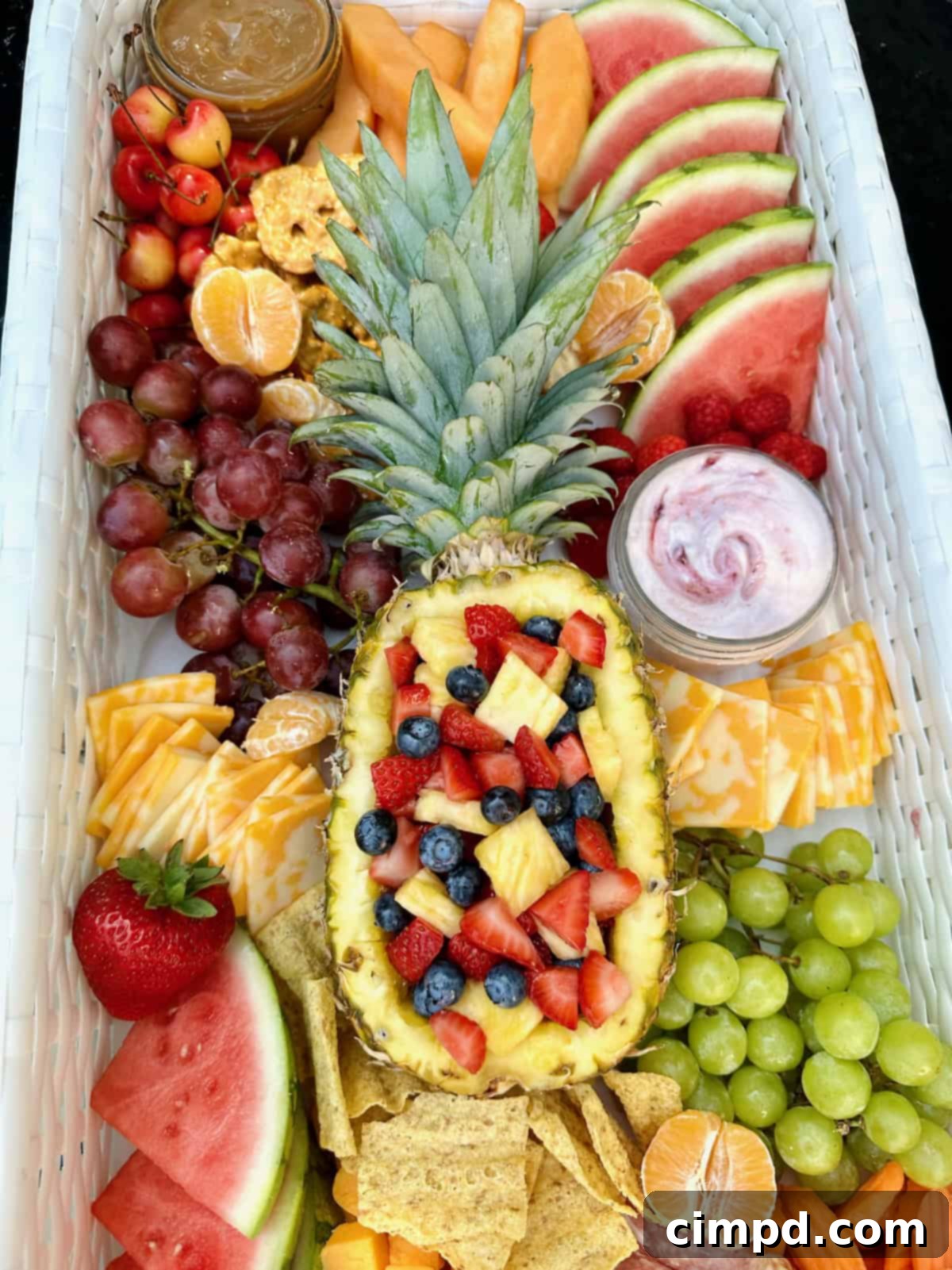 A close-up view of a floating snack tray in a pool, featuring a halved pineapple filled with berries as a centerpiece, surrounded by an assortment of fresh fruits, gourmet cheeses, and crispy crackers.