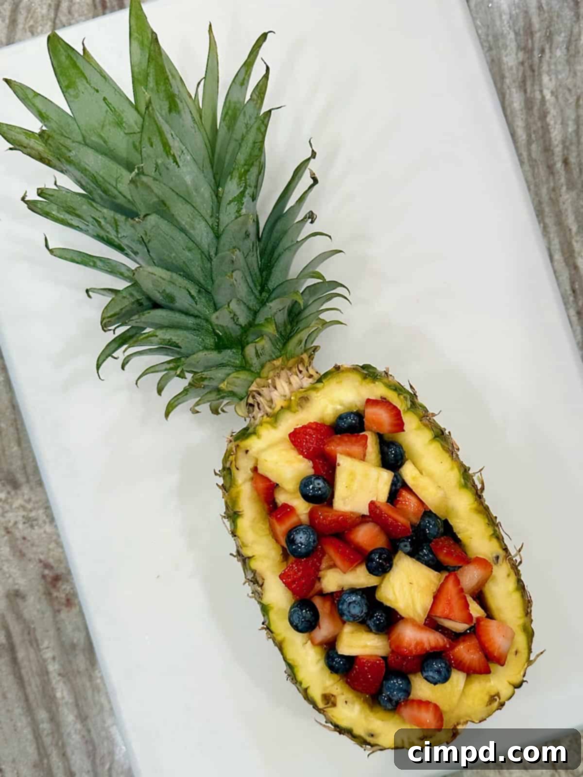 A vibrant pineapple boat, meticulously hollowed and filled with a colorful medley of whole blueberries, strawberry halves, and fresh pineapple chunks, presented beautifully on a flat surface.