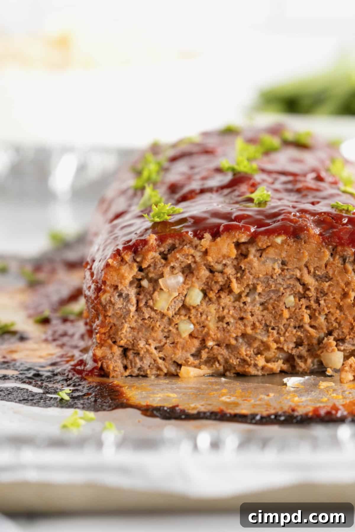 A freshly baked meatloaf, partially sliced to reveal its perfectly cooked interior, garnished with fresh parsley and resting on an aluminum foil-lined surface.