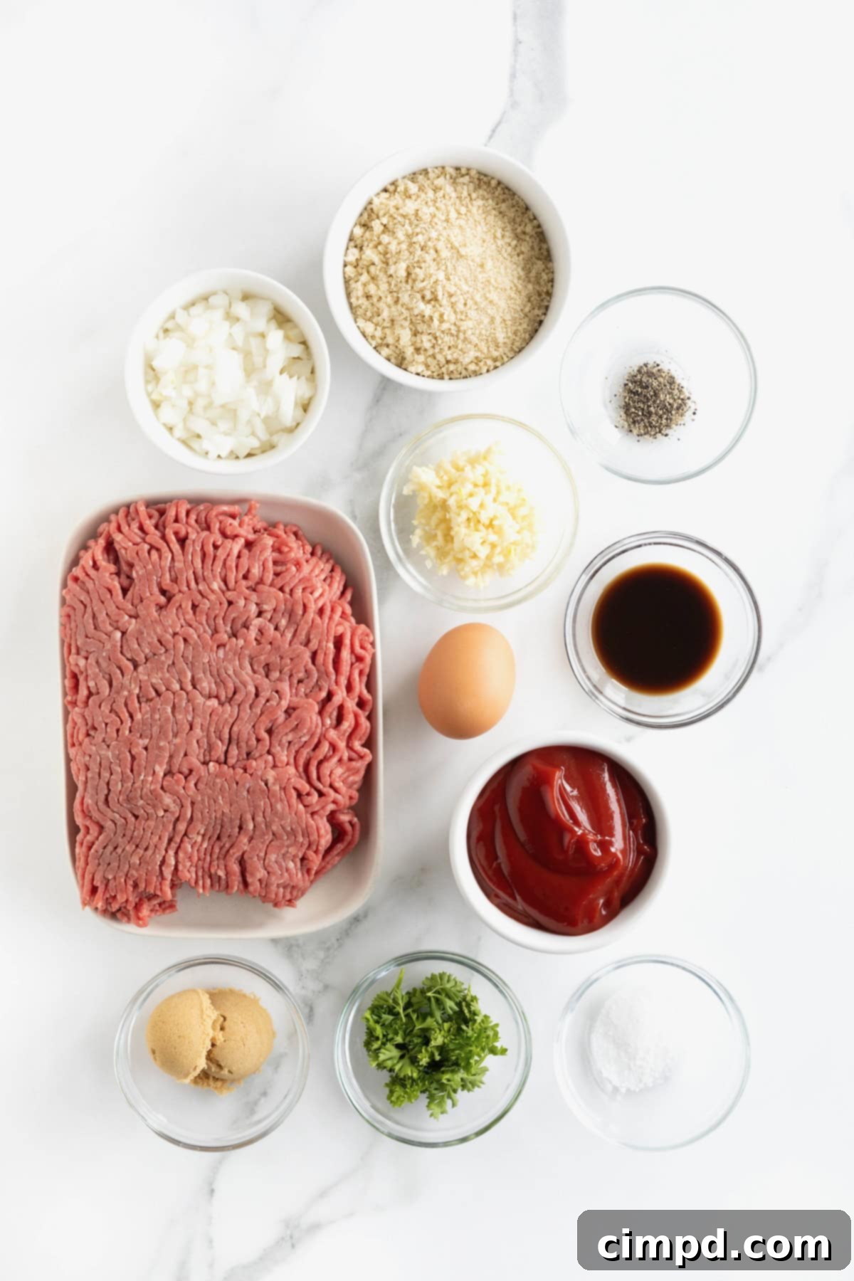 A selection of fresh ingredients laid out in small glass dishes on a pristine white marble counter, ready for making classic meatloaf.