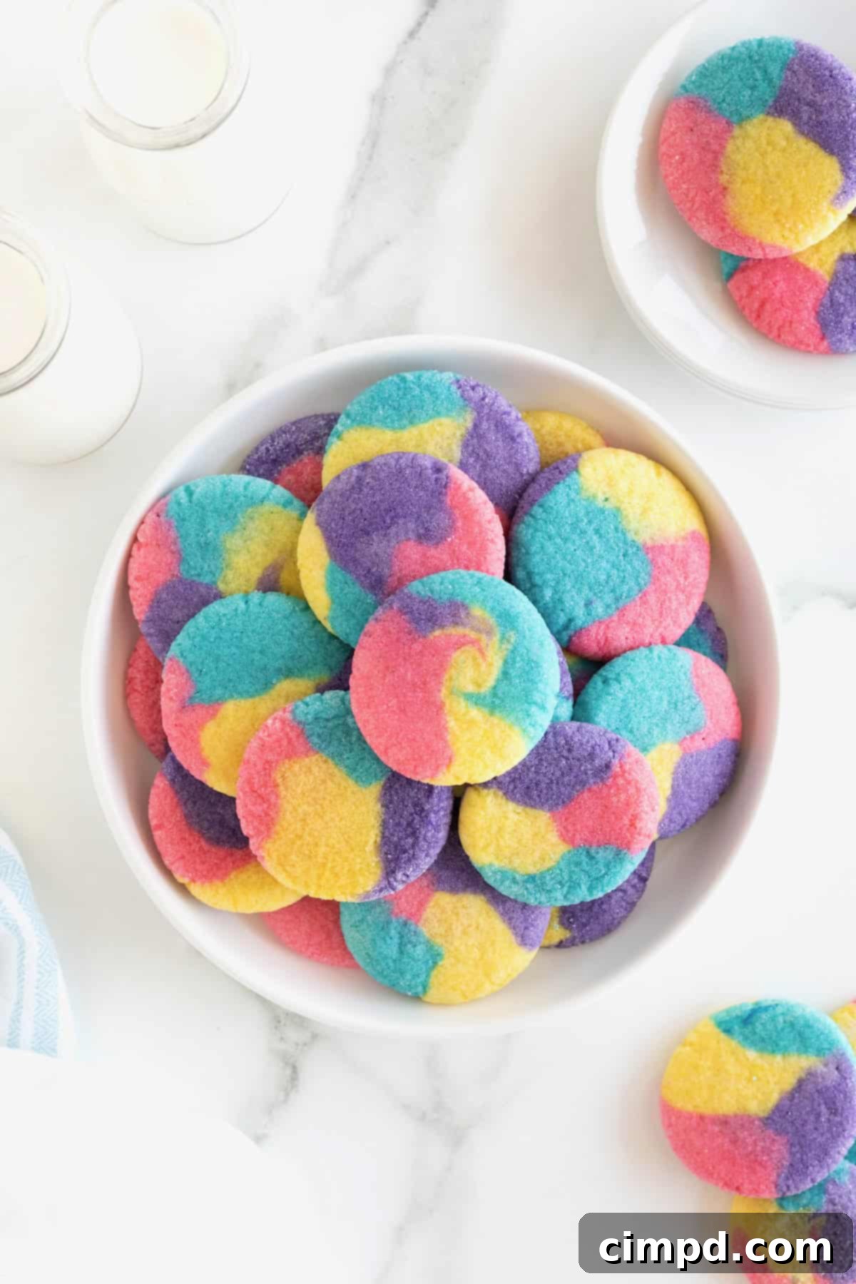 Vibrant Swirl Sugar Cookies 2 A large serving plate stacked with colorful sugar cookies with pink, purple, blue and yellow swirls in them, showcasing their vibrant tie-dye pattern.