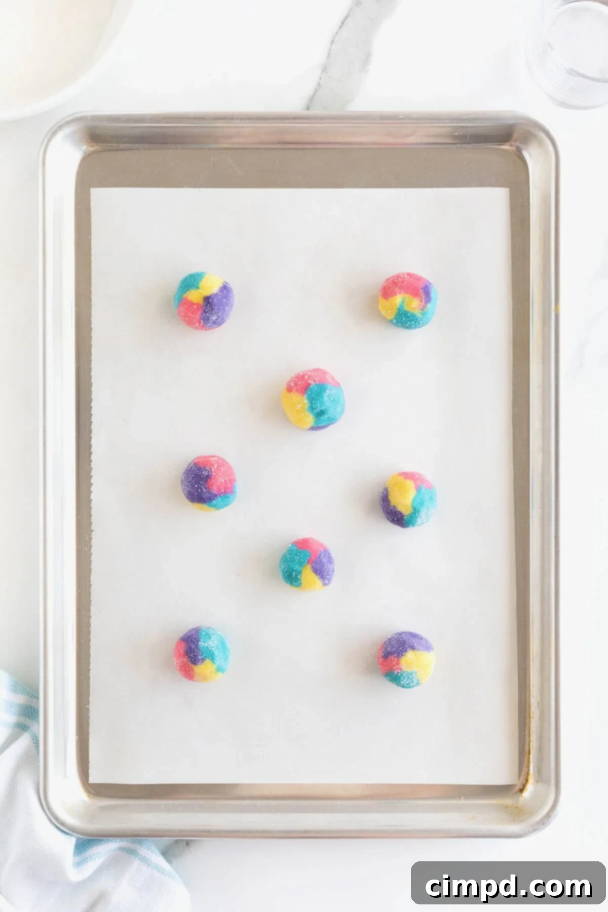 Vibrant Swirl Sugar Cookies 8 Eight perfectly formed multicolored cookie dough balls, each with vibrant swirls, arranged on a parchment-lined aluminum baking sheet, ready for the oven.