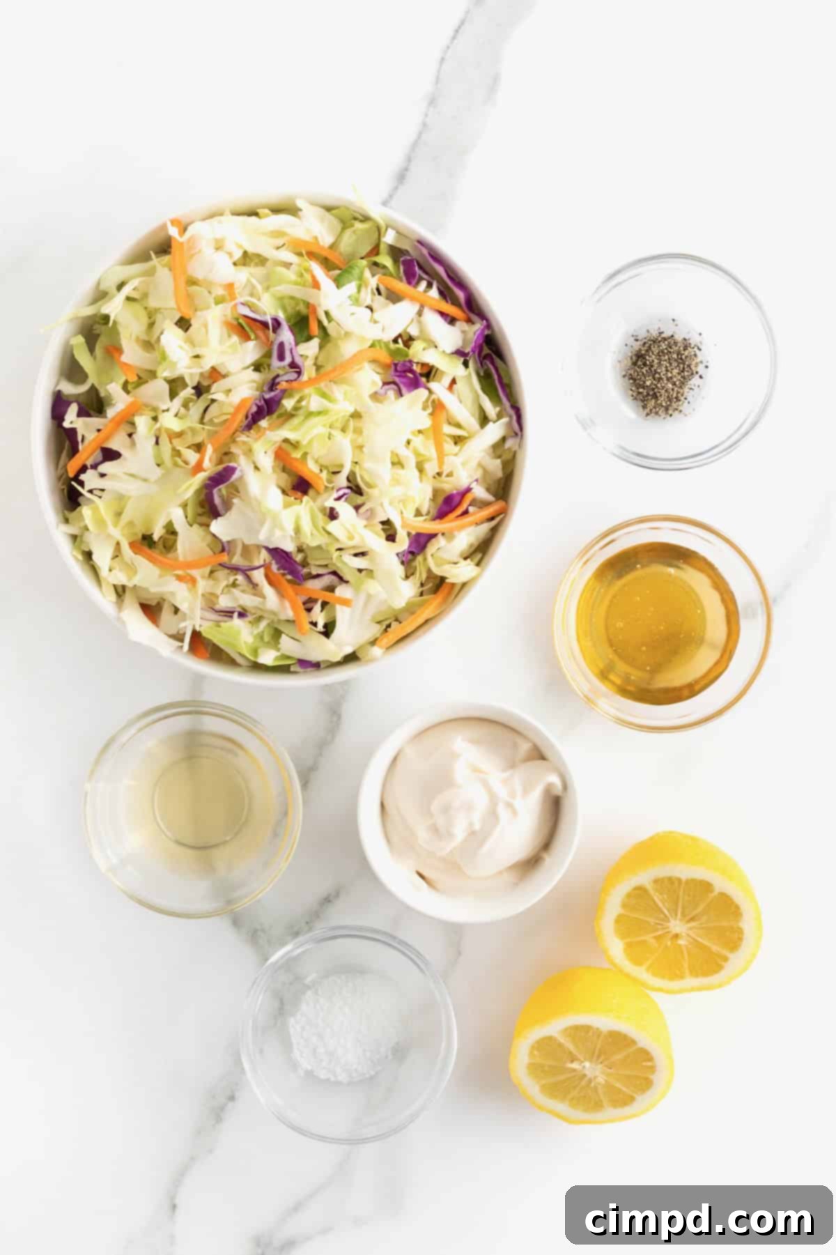 A large glass mixing bowl filled with colorful coleslaw mix, alongside small glass dishes holding the individual ingredients for the dressing.