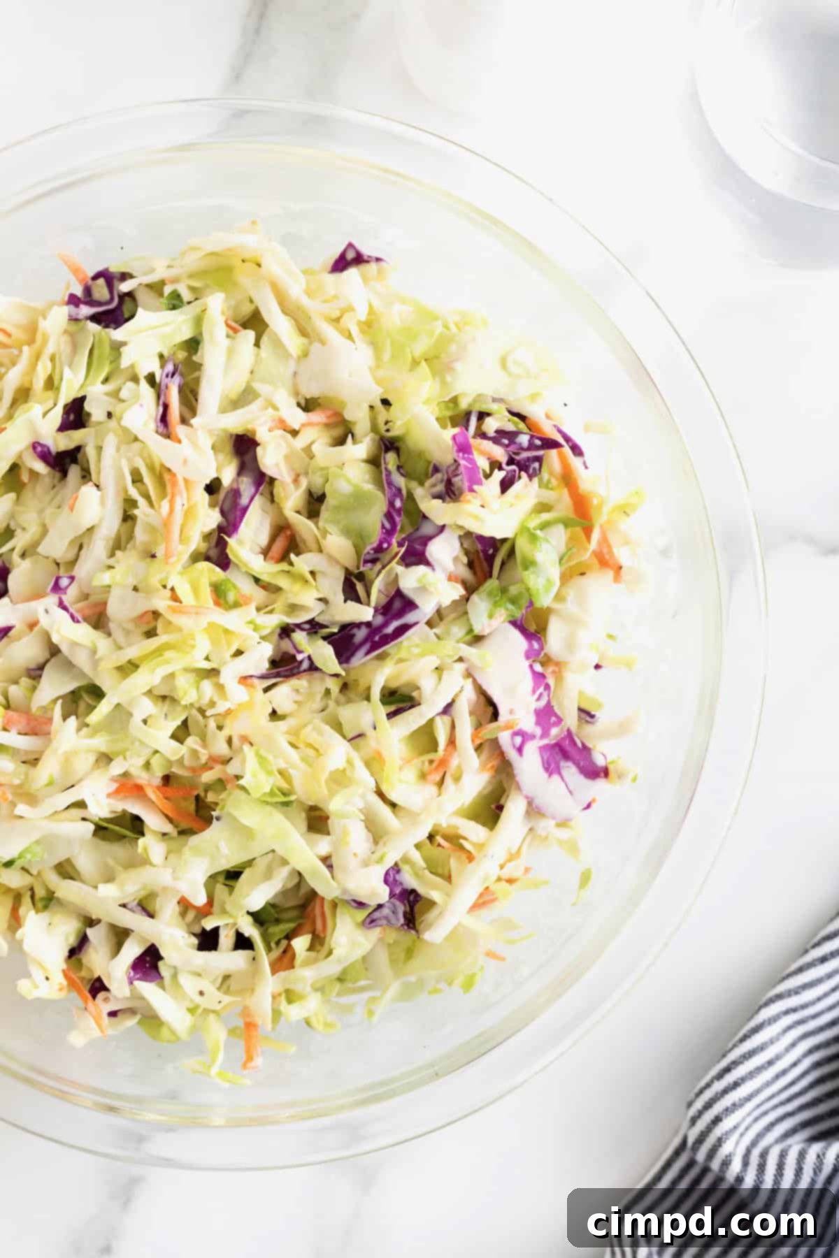 A large glass bowl of classic coleslaw ready for serving on a white marble counter.