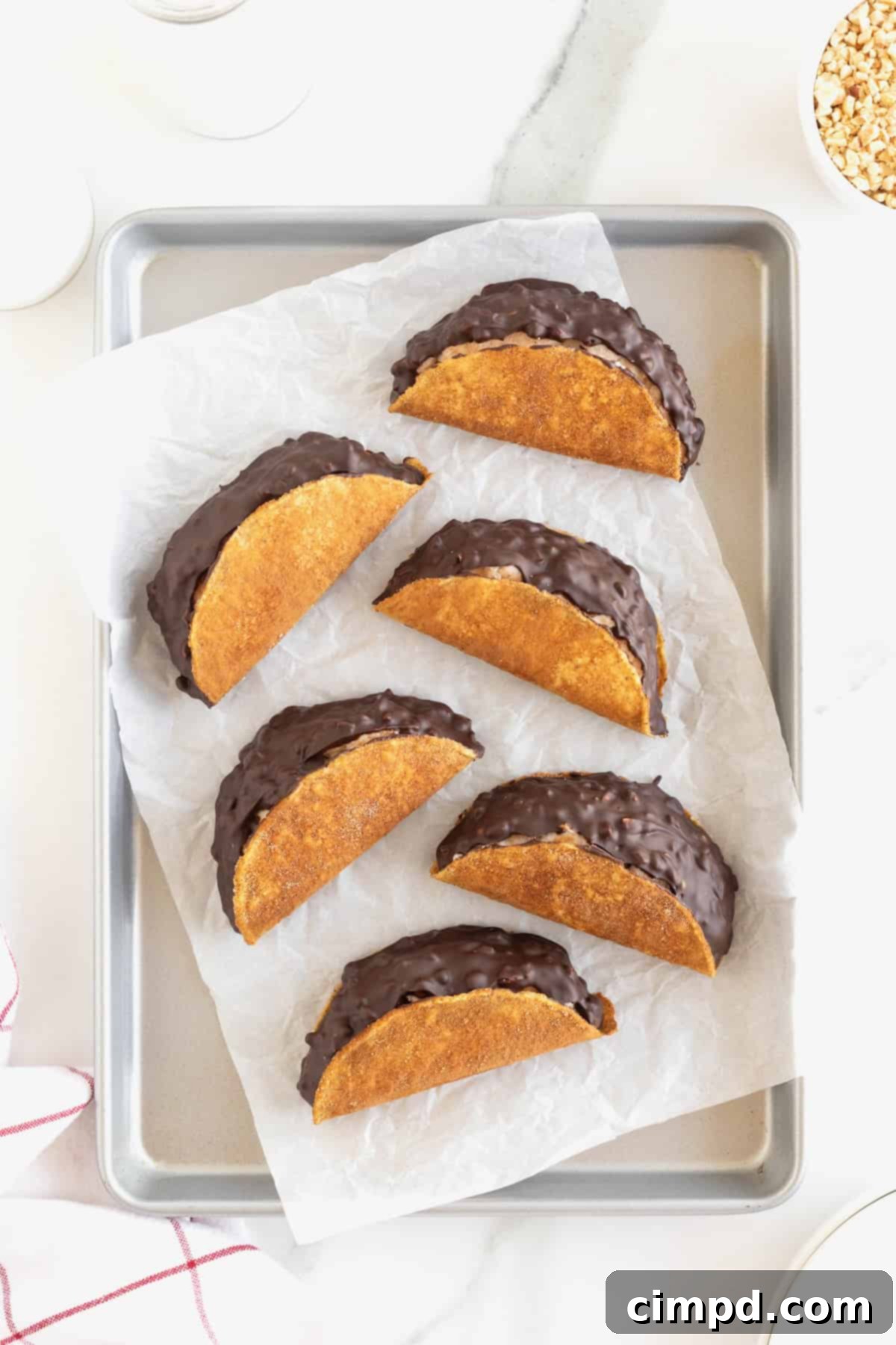 Frozen Chocolate Taco Treats 11 A batch of six homemade choco tacos, perfectly finished and frozen, displayed on a parchment-lined aluminum baking sheet.