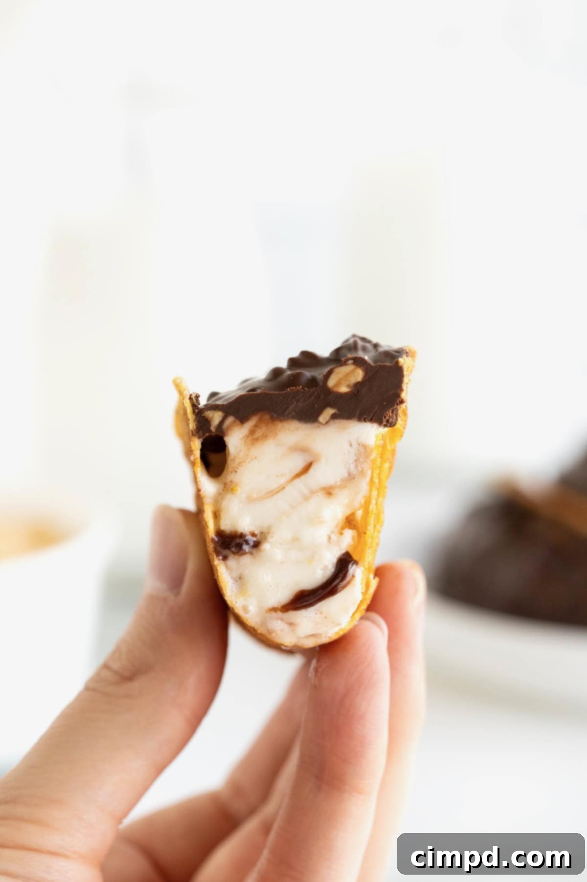 Frozen Chocolate Taco Treats 3 A hand holding a freshly made homemade choco taco, with a bite taken out to reveal the rich fudge ripple ice cream inside.