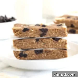 Sunrise Blueberry Banana Almond Bars 10 Three blueberry banana almond breakfast bars stacked on a white rimmed plate with pieces of parchment between them.