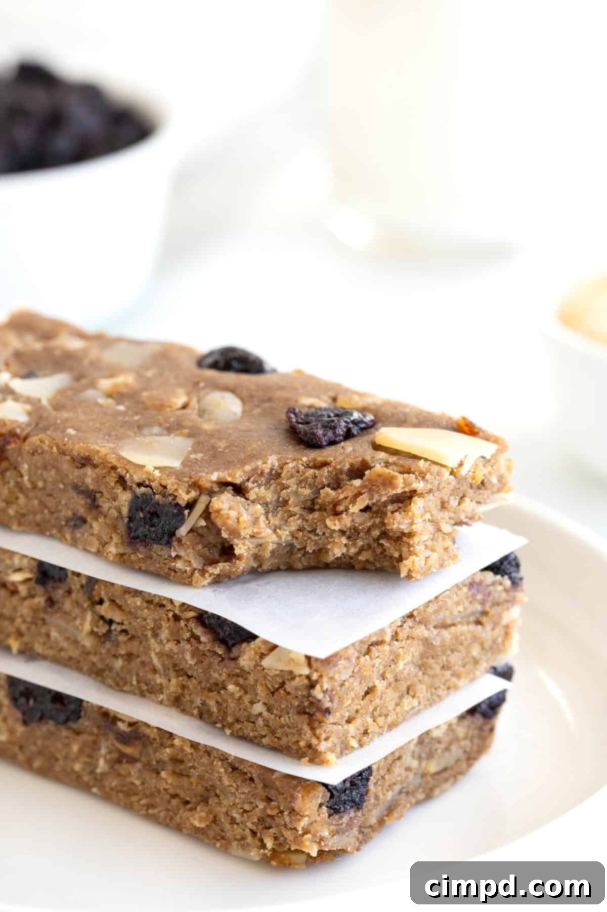 Sunrise Blueberry Banana Almond Bars 4 A close-up of three stacked blueberry banana almond breakfast bars, with a bite taken from the top one, revealing the rich, textured interior.