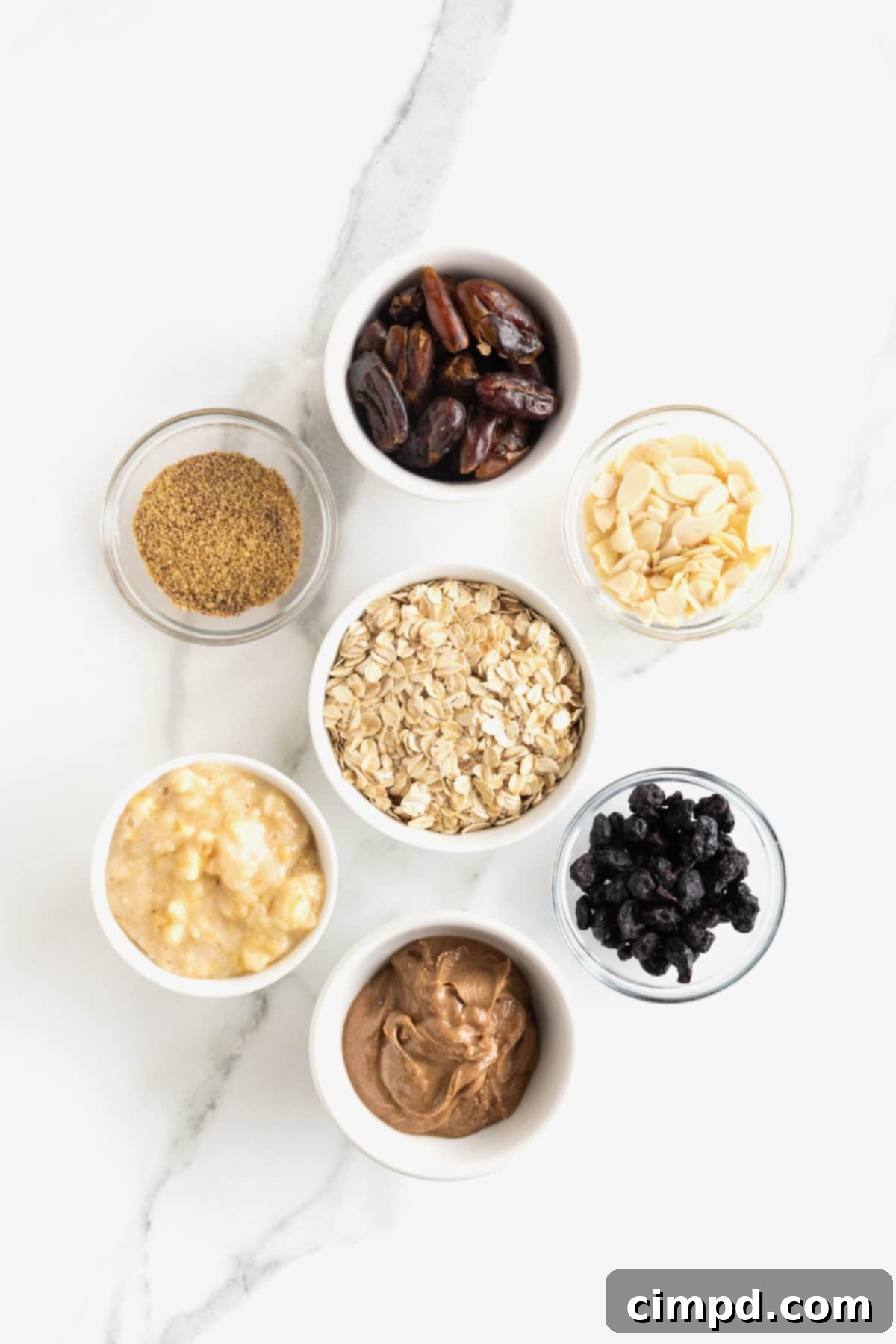 Sunrise Blueberry Banana Almond Bars 5 A beautiful flat lay of ingredients for Blueberry Banana Almond Breakfast Bars, neatly arranged in small glass dishes on a pristine white marble counter, showcasing their freshness and quality.