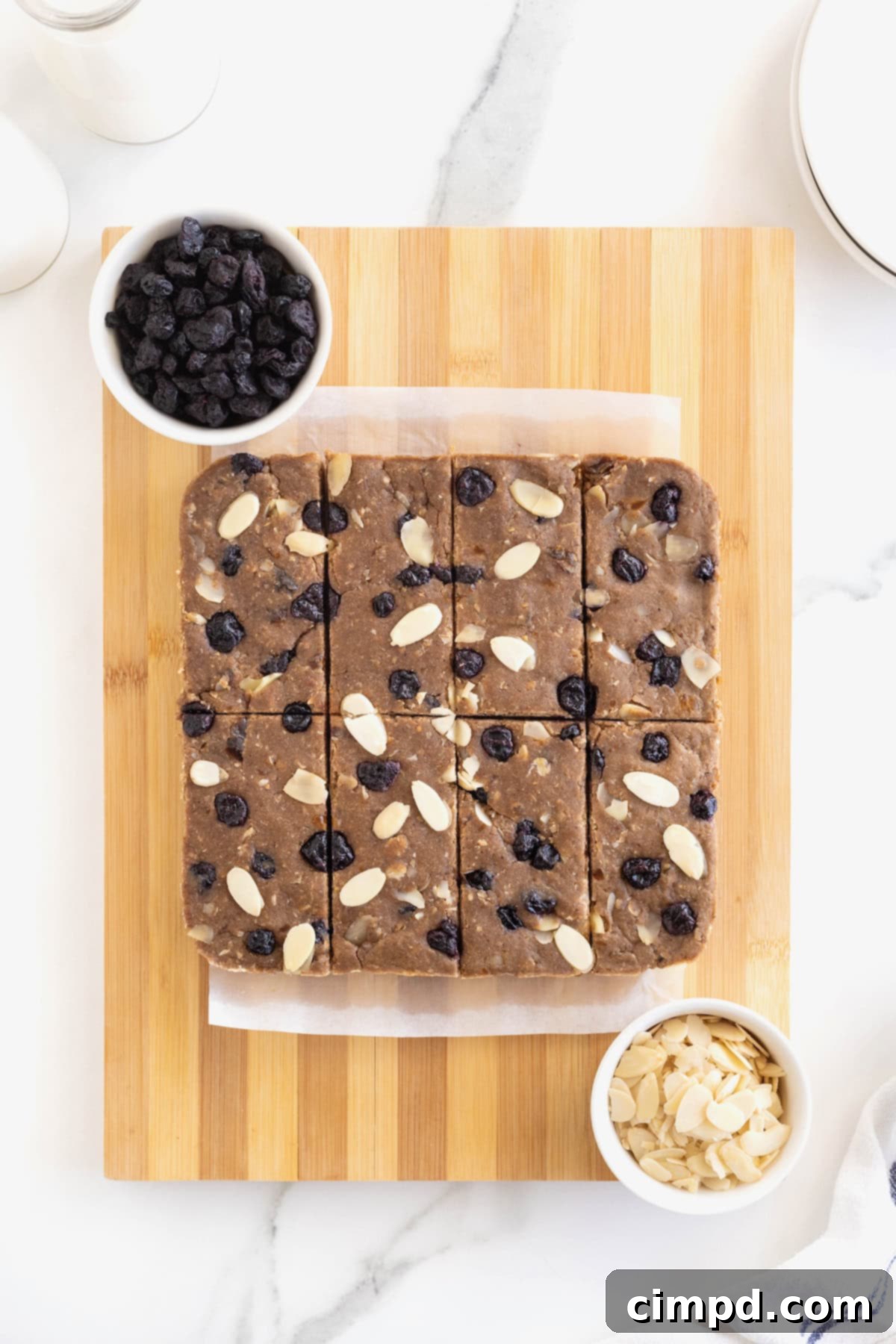 Sunrise Blueberry Banana Almond Bars 8 Perfectly cut breakfast bars, topped with sliced almonds and blueberries, arranged on a parchment-lined wooden cutting board, showcasing their ready-to-eat form.